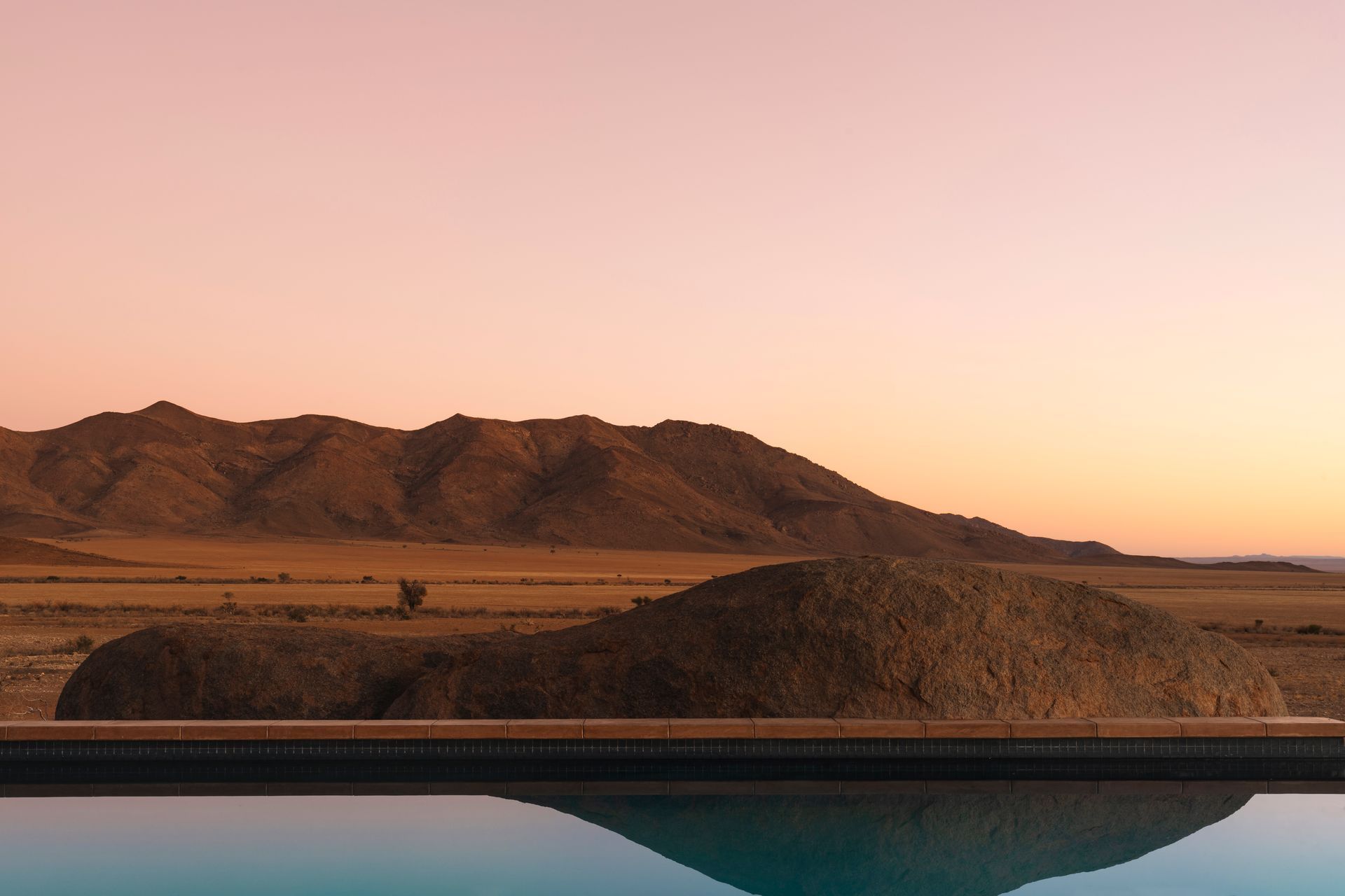 A swimming pool at a desert camp with mountains in the background at sunset in Namibia, Africa.