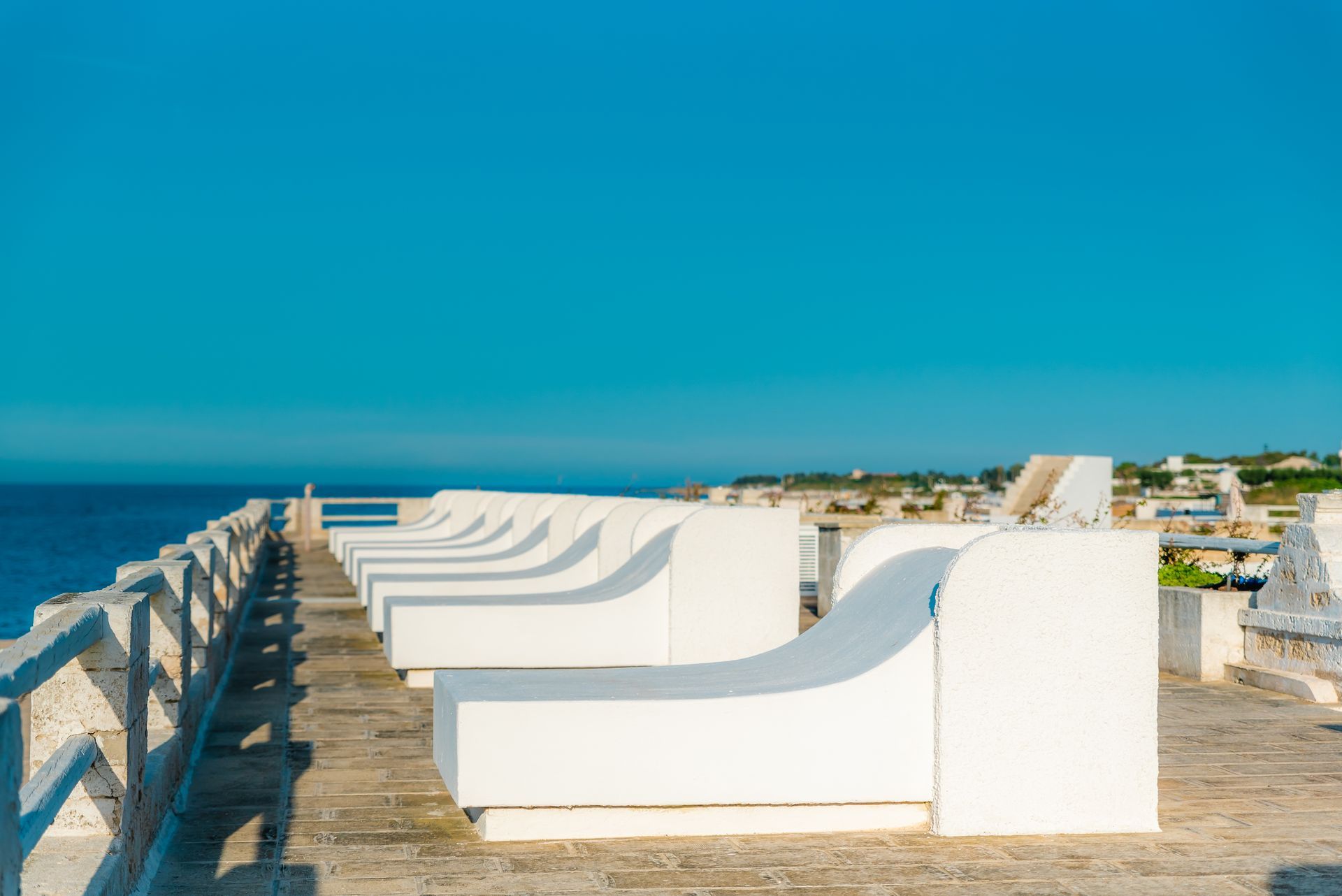 A row of white lounge chairs on a pier overlooking the ocean at La Peschiera Hotel in Puglia, Italy.