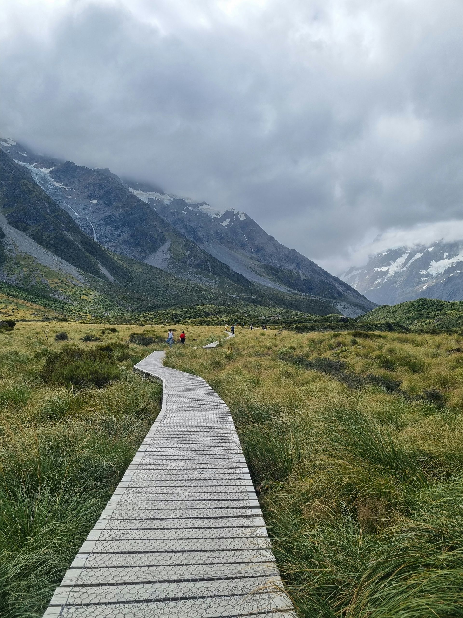 A wooden walkway going through a grassy field with Mount Cook in the background on the Hooker Valley track, New Zealand.