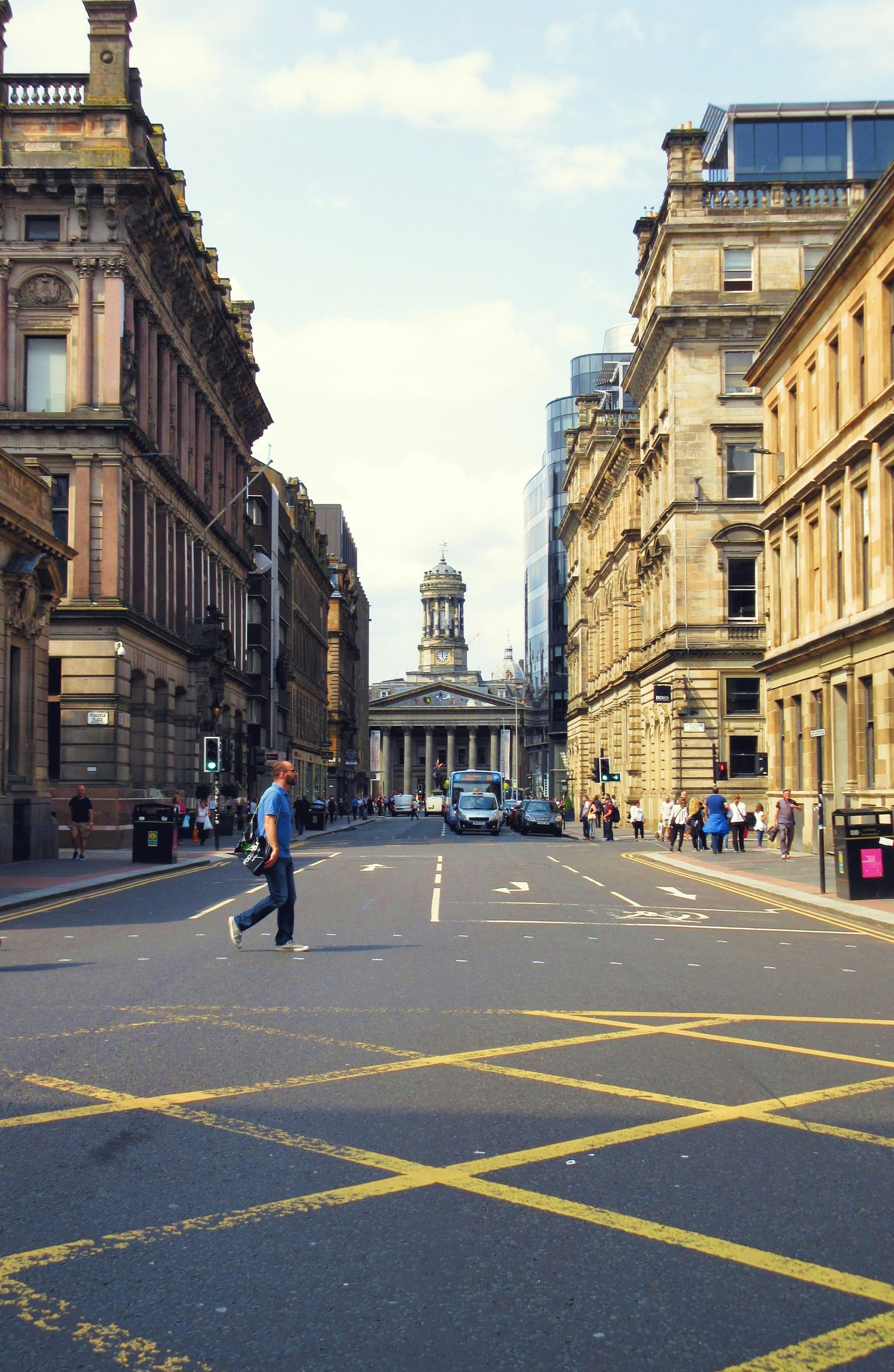 Street view in Glasgow, Scotland; man crossing street; classical building in distance; buildings on either side.