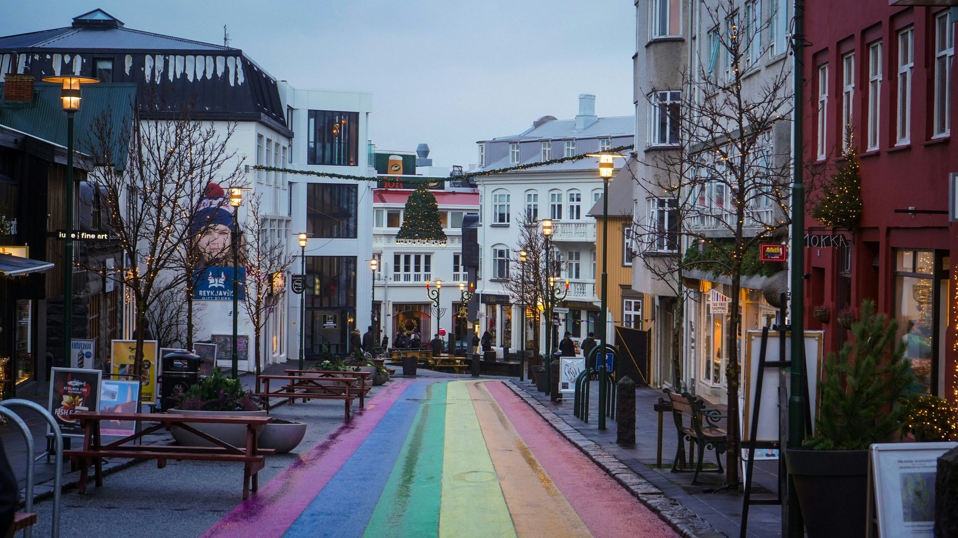A rainbow-colored street lined with buildings, trees, and benches in Reykjavík, Iceland.