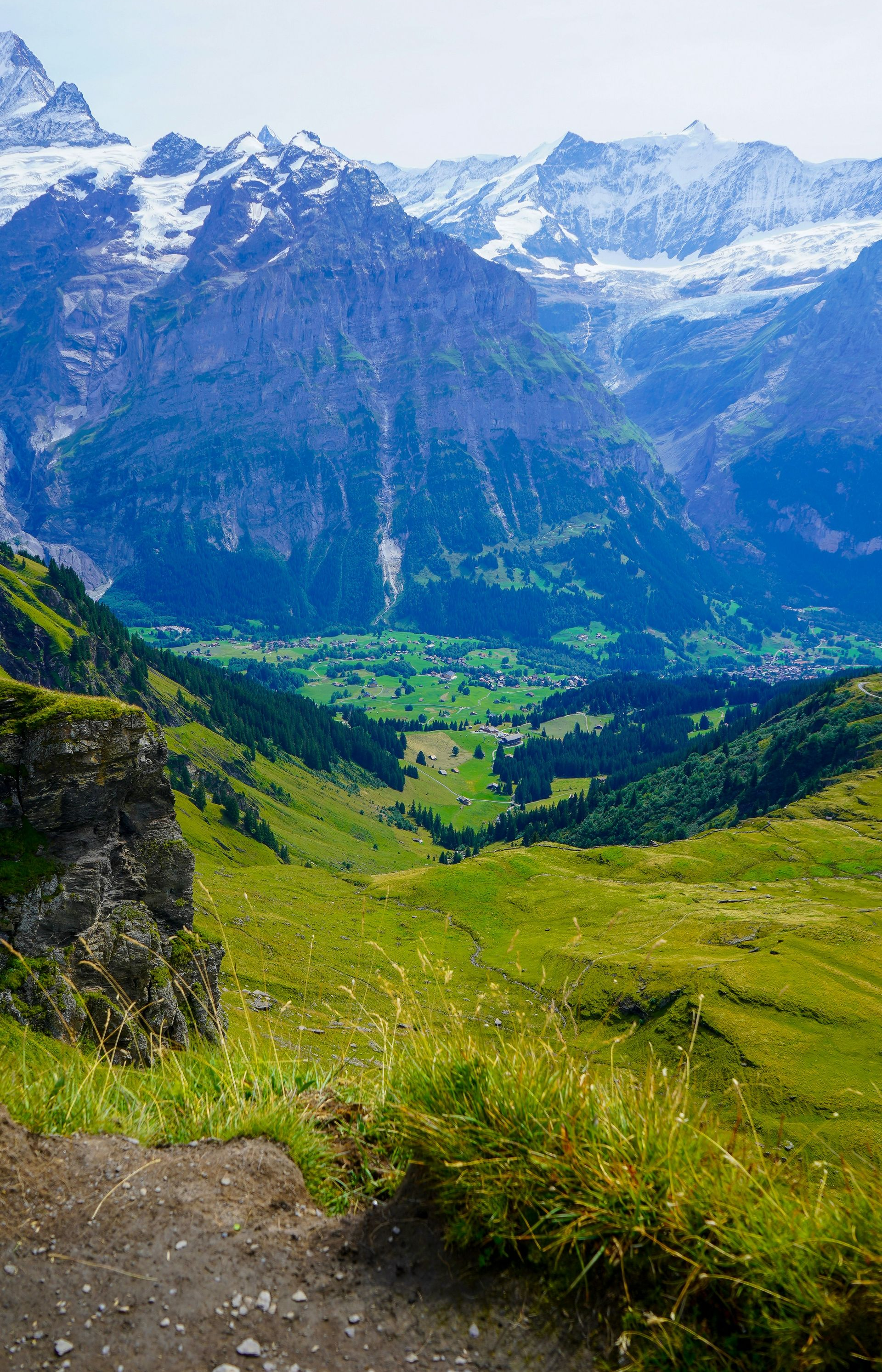 Green valley nestled between snow-capped mountains under a bright sky in Interlaken, Switzerland.