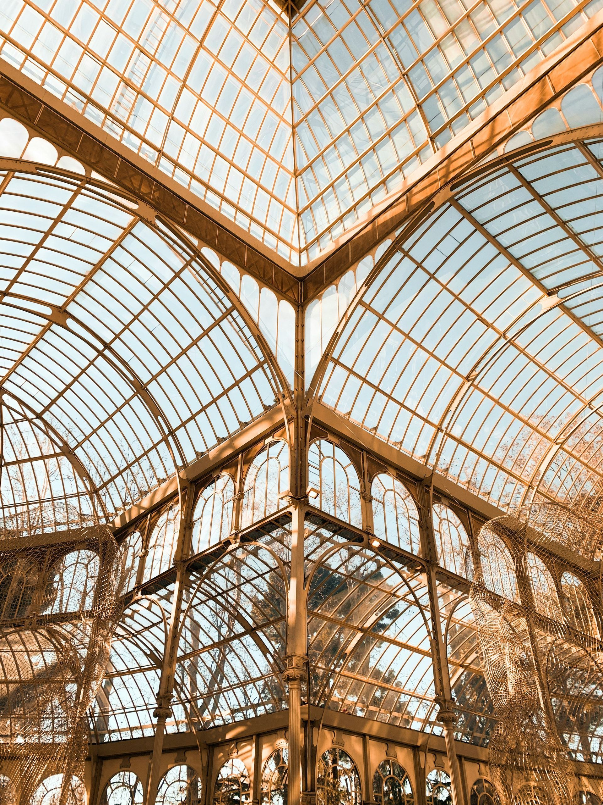 Ornate glass ceiling and arches, golden hues, looking up into a blue sky in Madrid, Spain.