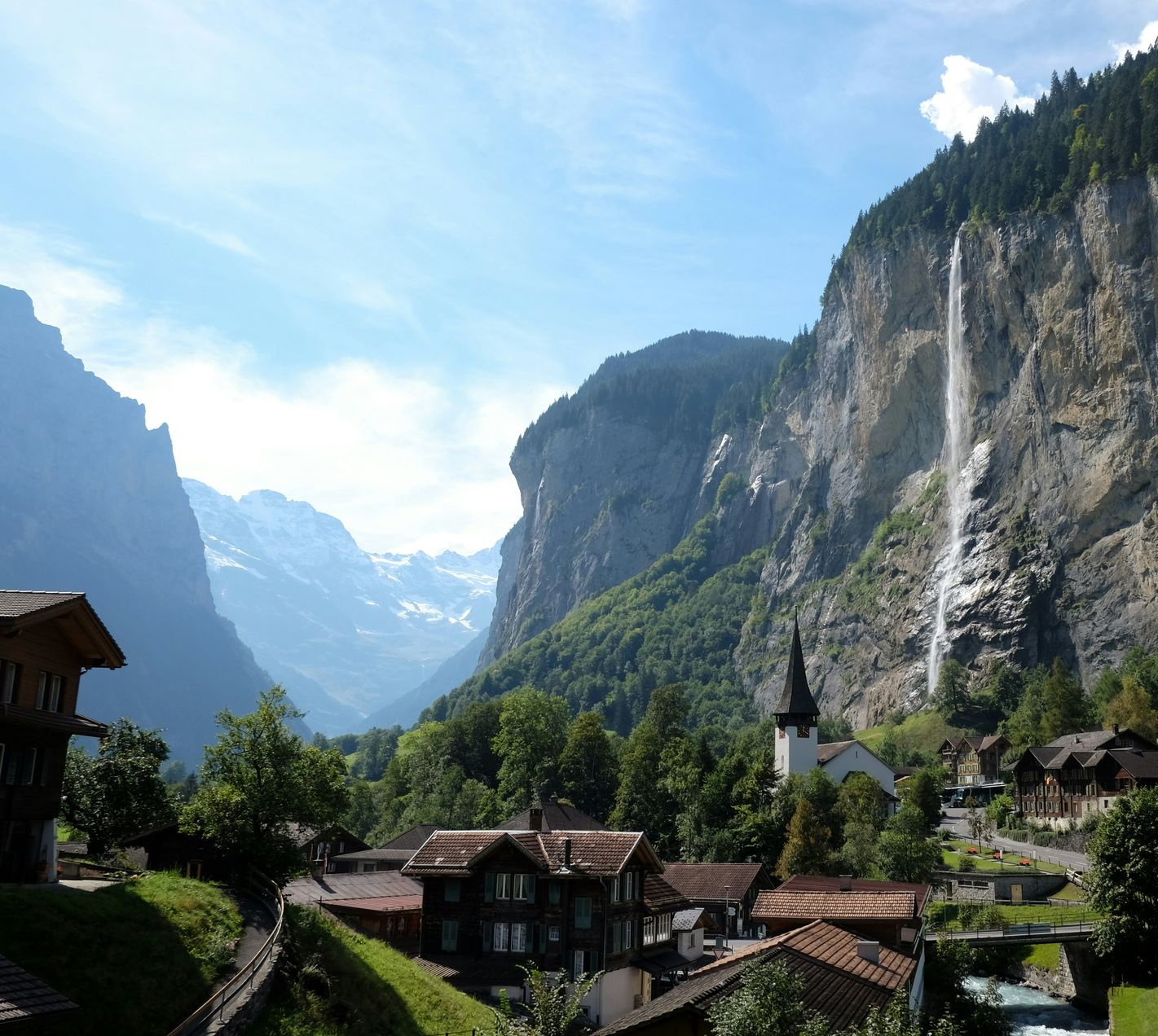 Lauterbrunnen village nestled in a Swiss valley with a waterfall cascading down a rocky cliff under a blue sky.