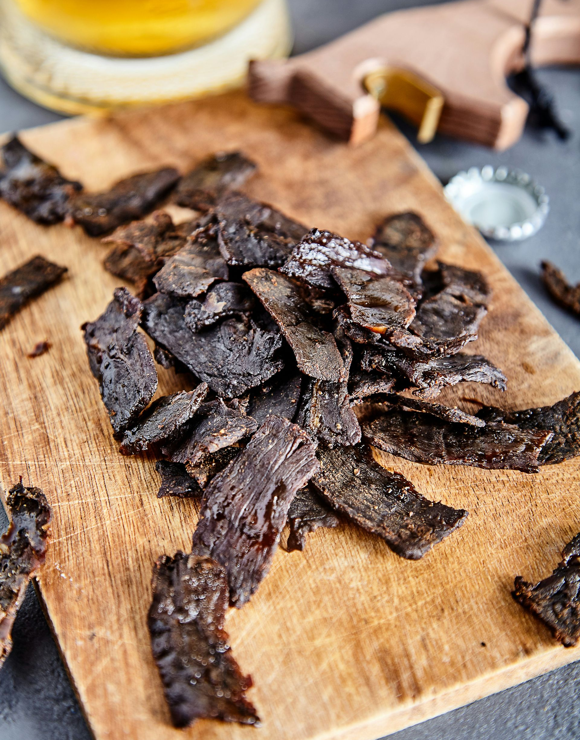 Traditionl Biltong - dried beef piled on a wooden cutting board, next to a bottle cap and beer in Namibia.