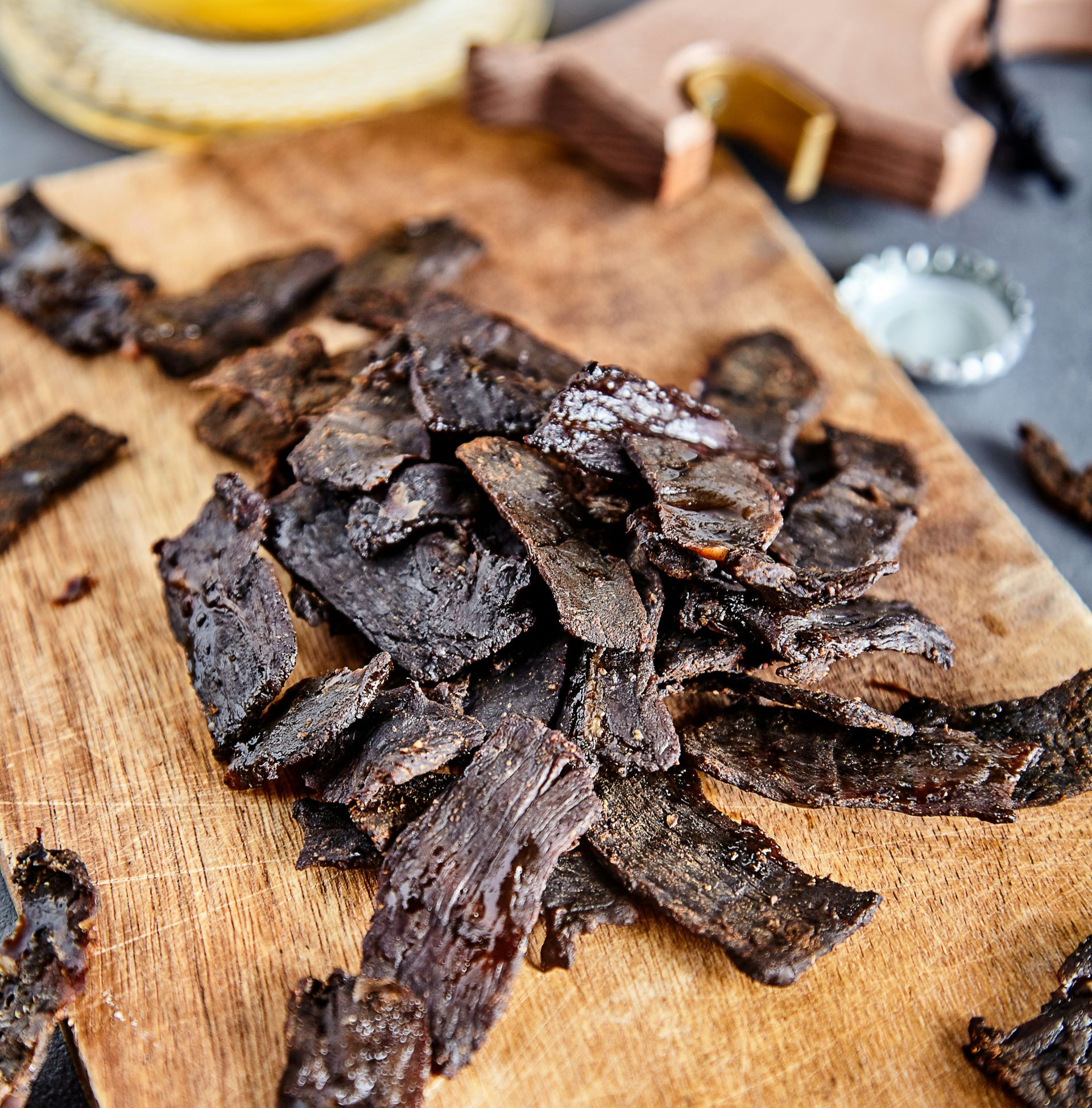 Traditionl Biltong - dried beef piled on a wooden cutting board, next to a bottle cap and beer in Namibia.