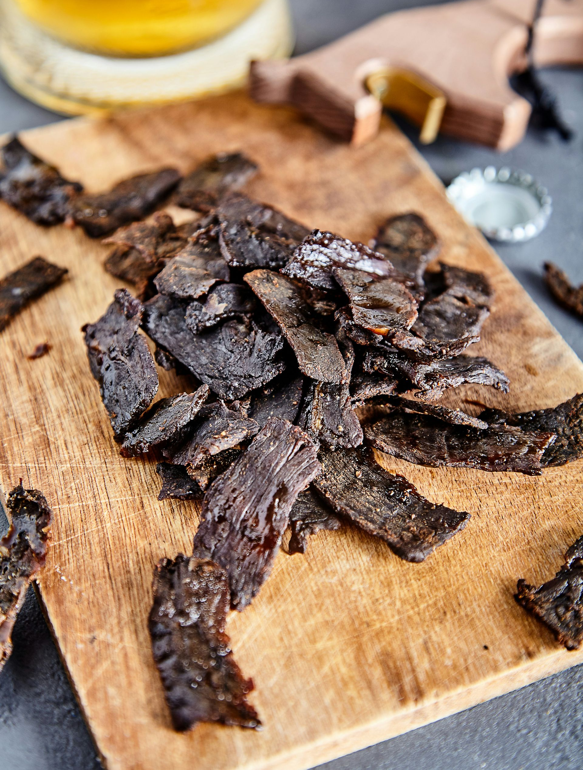 Traditionl Biltong - dried beef piled on a wooden cutting board, next to a bottle cap and beer in Namibia.