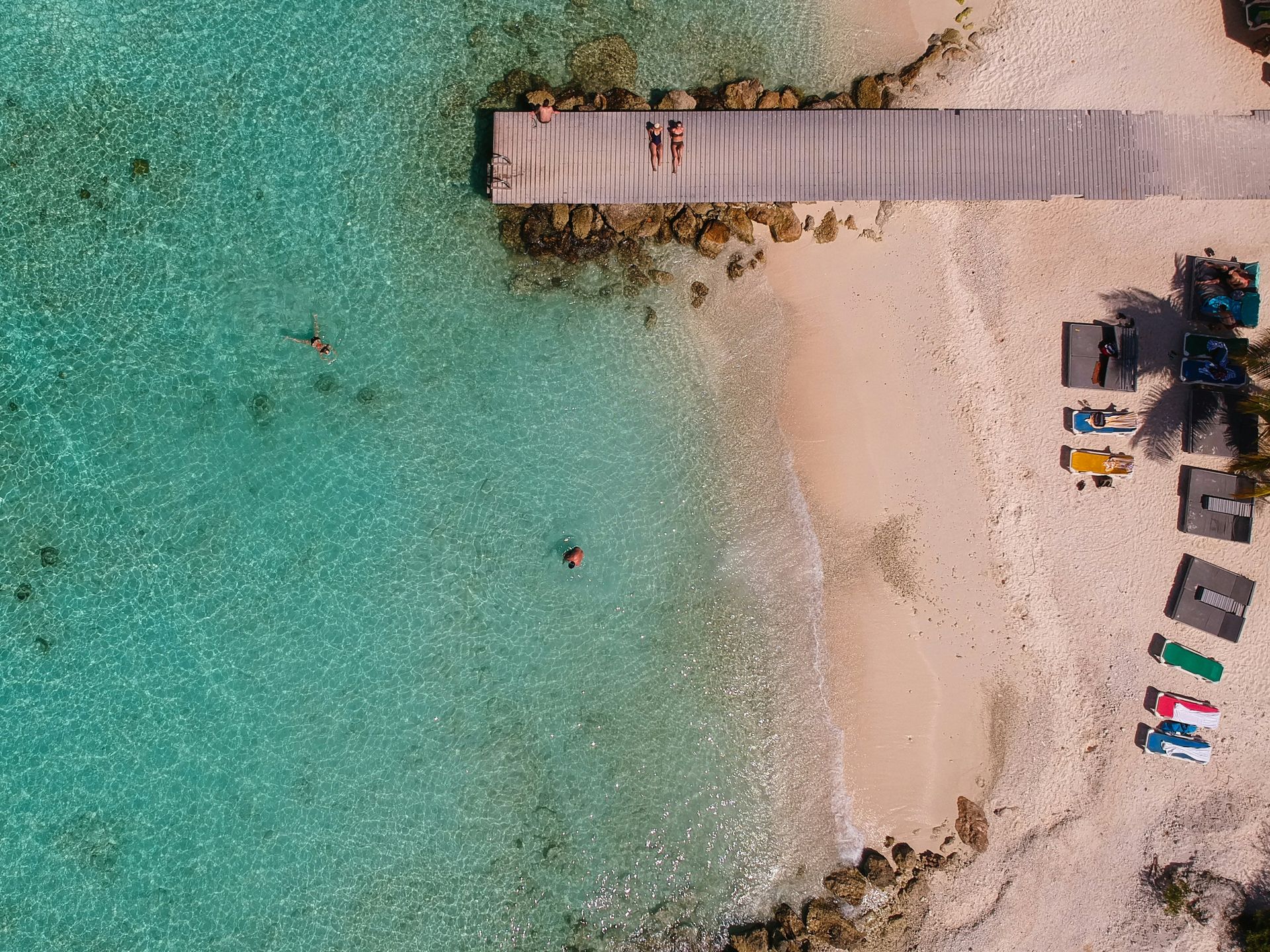 An aerial view of a beach with a dock and people swimming in the water in the Caribbean.