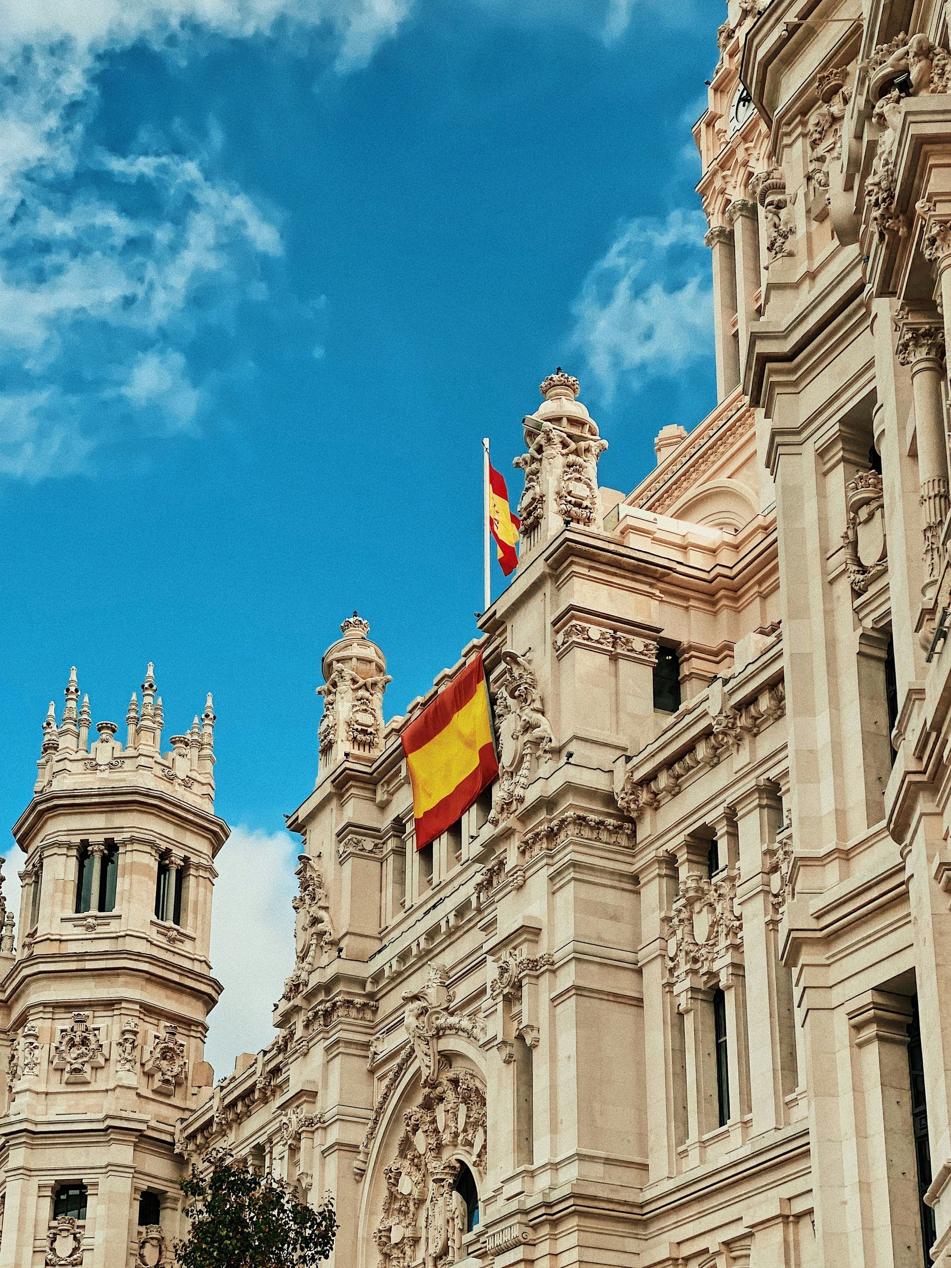 Ornate white building with Spanish flag against a blue sky with clouds in Madrid, Spain.