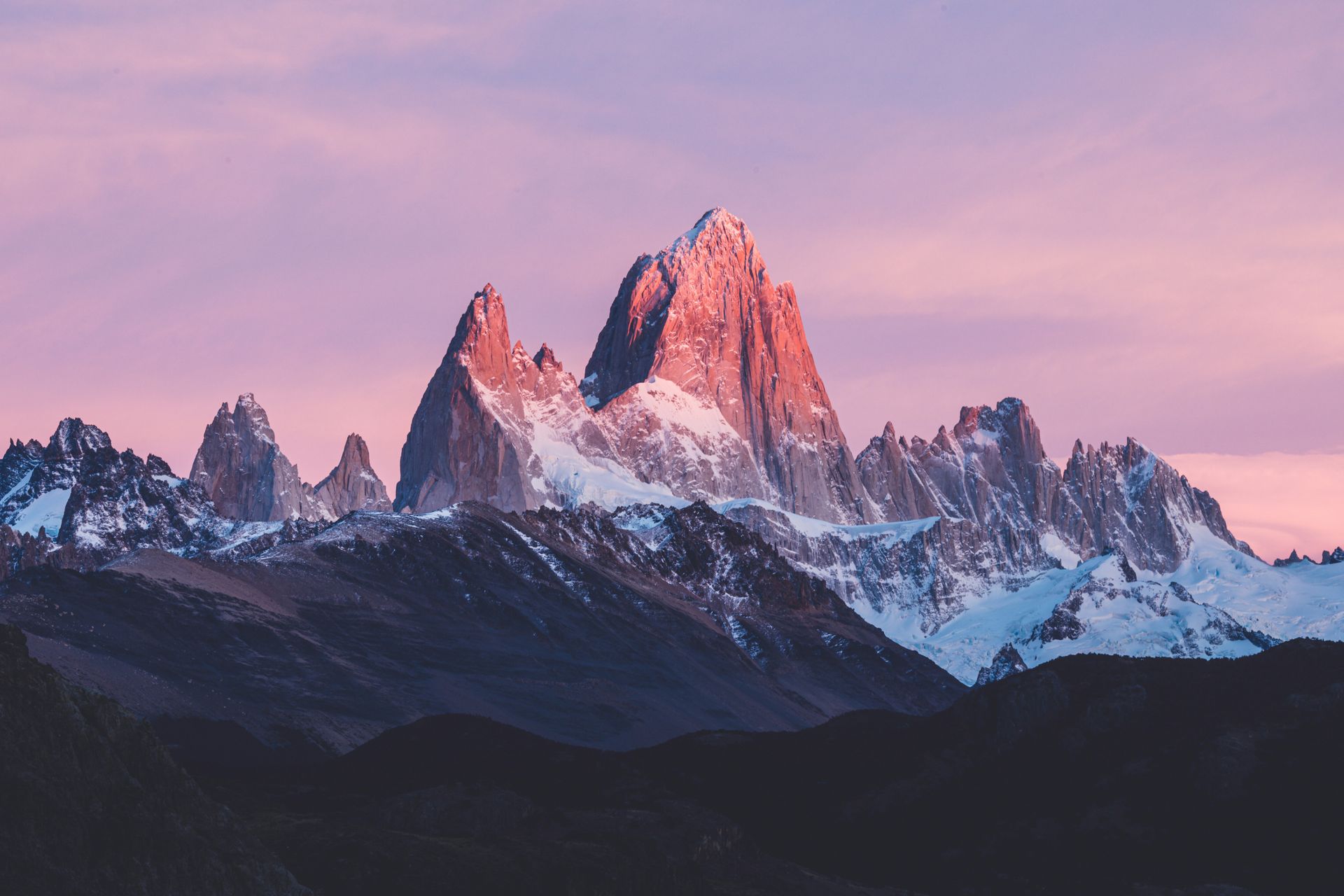 Snow-capped mountain peaks glow pink at sunset, set against a purple and pink sky in Patagonia, Argentina.