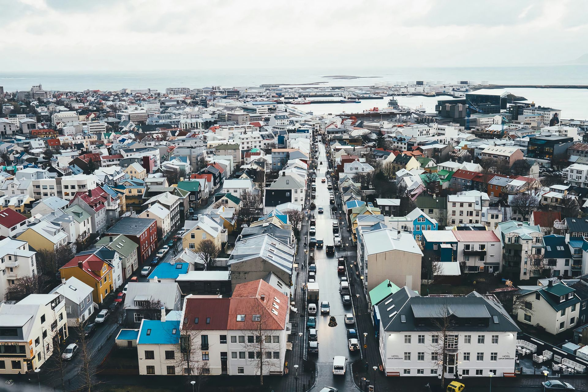 Aerial view of the colorful city of Reykjavík with buildings and roads, overlooking the ocean on a cloudy day.