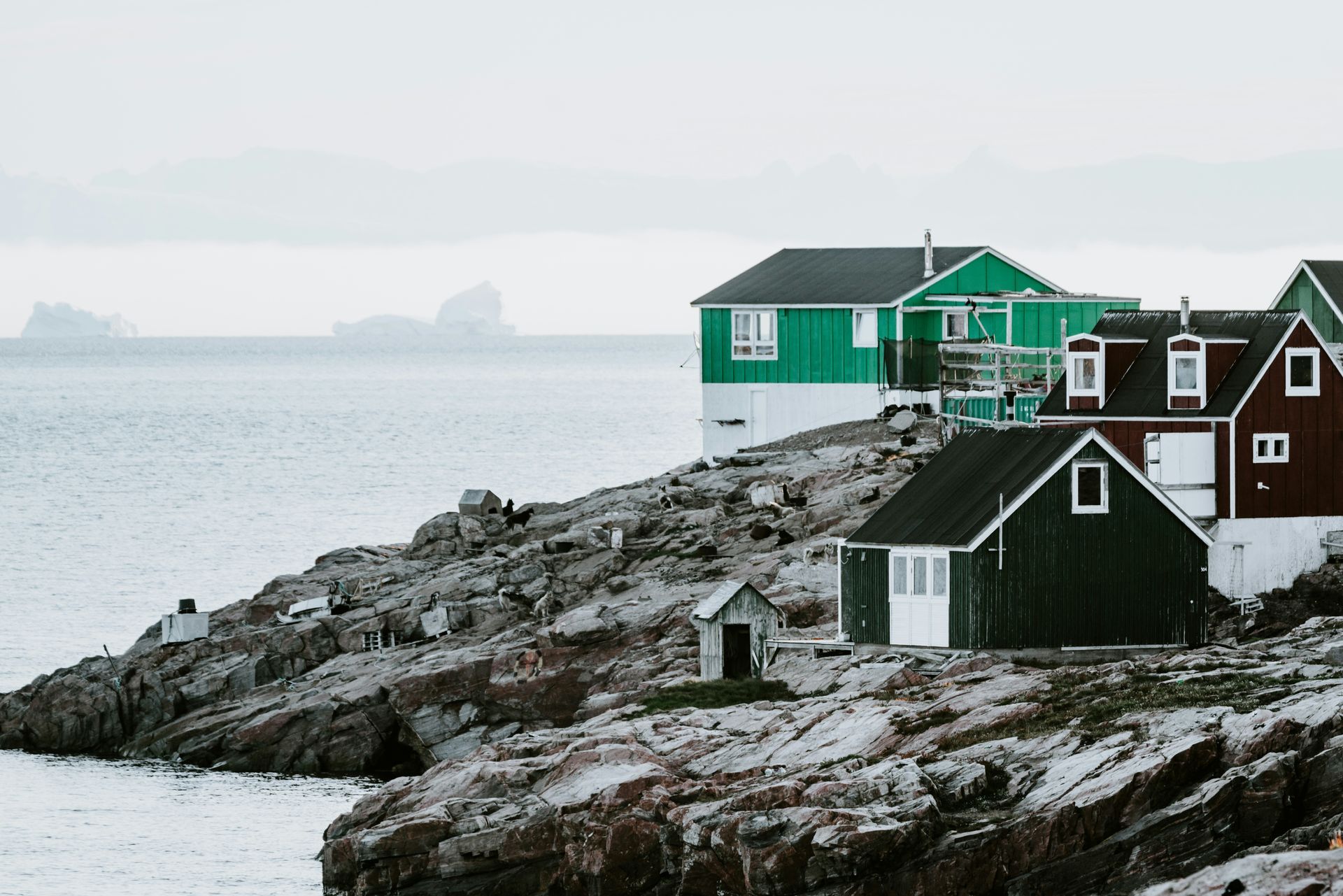 Houses, painted green and red, sit on a rocky coast in Ittoqqortoormiit, Greenland.
