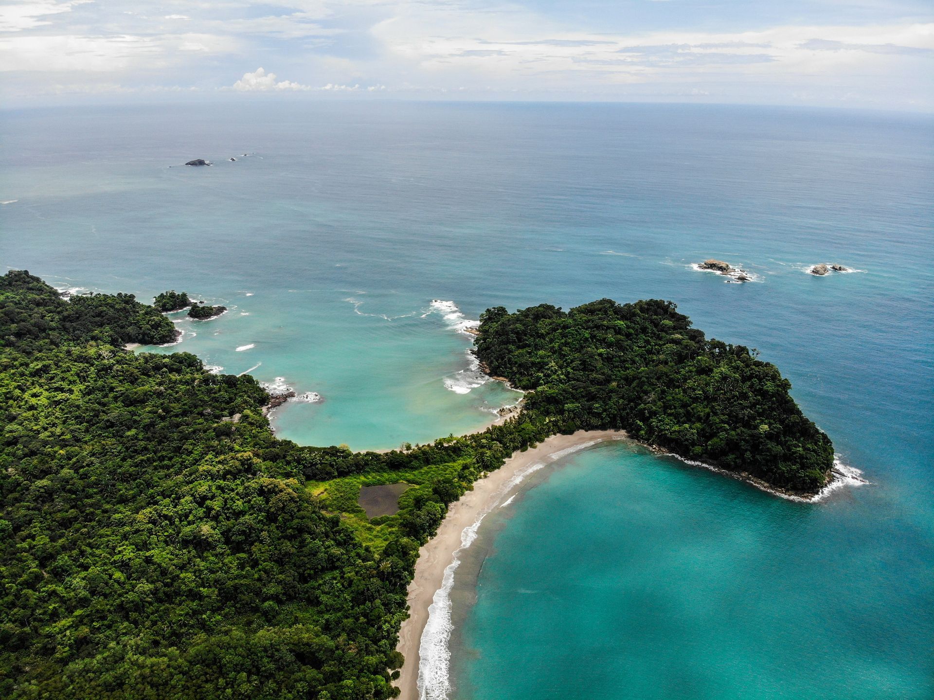 Aerial view of a tropical coastline with a turquoise beach and dense green jungle in Manuel Antonio, Costa Rica.
