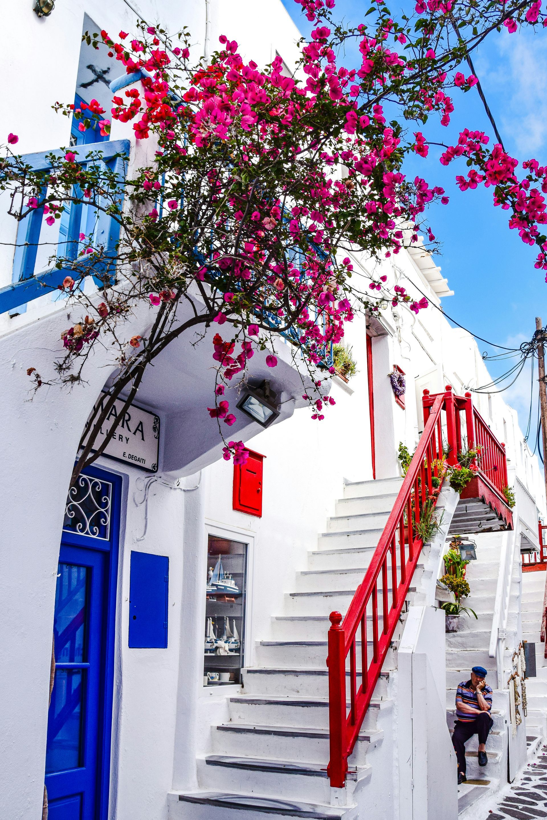 A white building with red stairs and pink flowers in Mykonos, Greece.