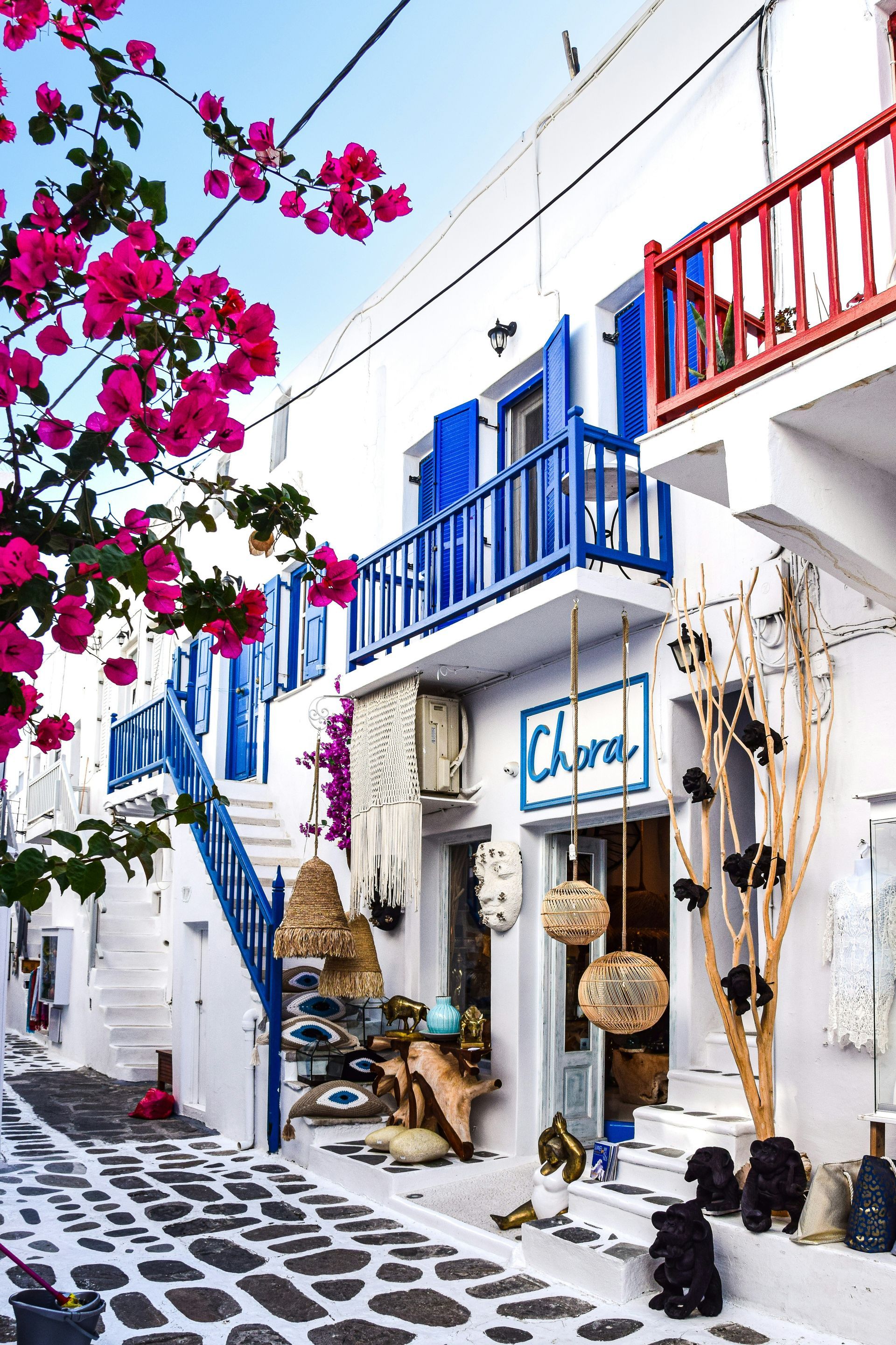 A white building with blue shutters and pink flowers in front of it in Mykonos, Greece.