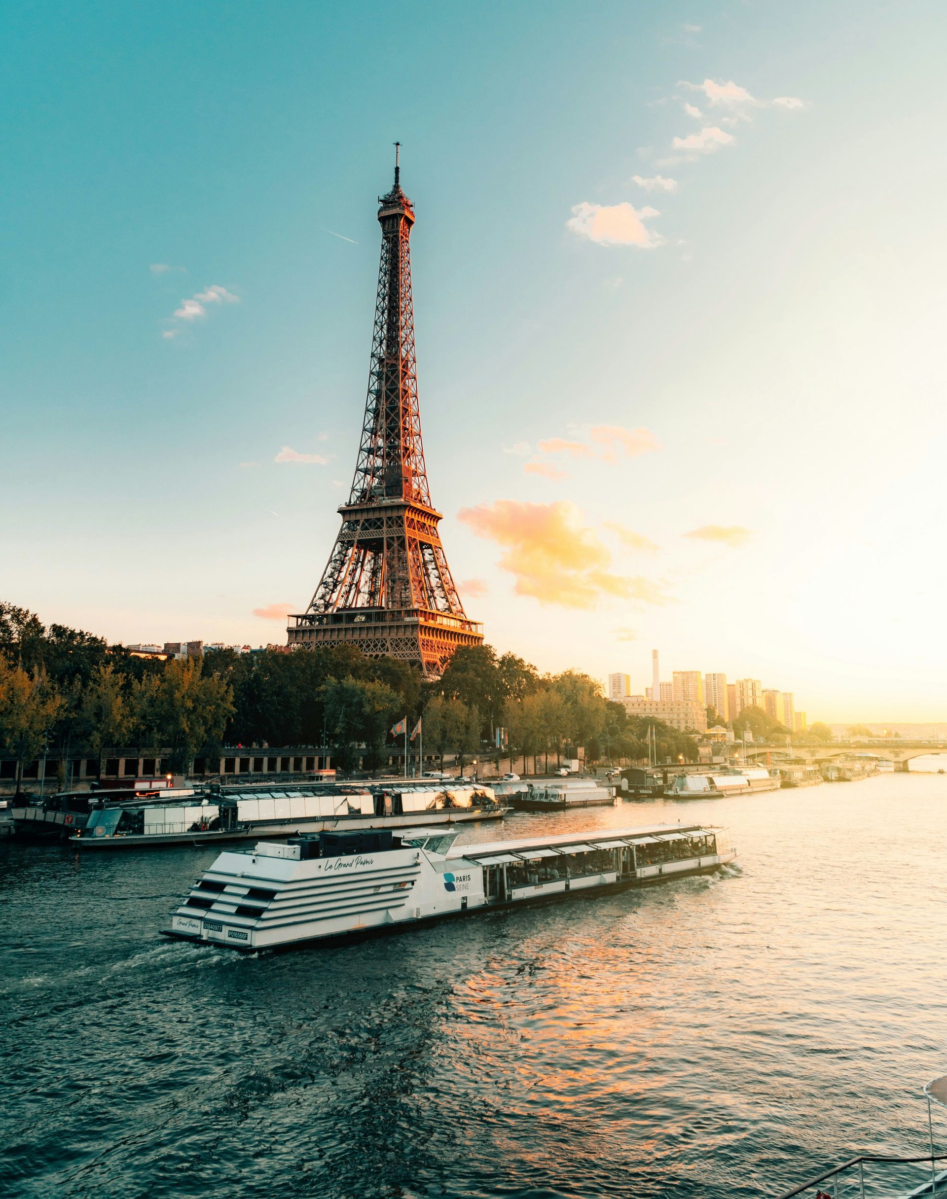 Eiffel Tower in Paris at sunset with a river cruise ship sailing on the Seine River.