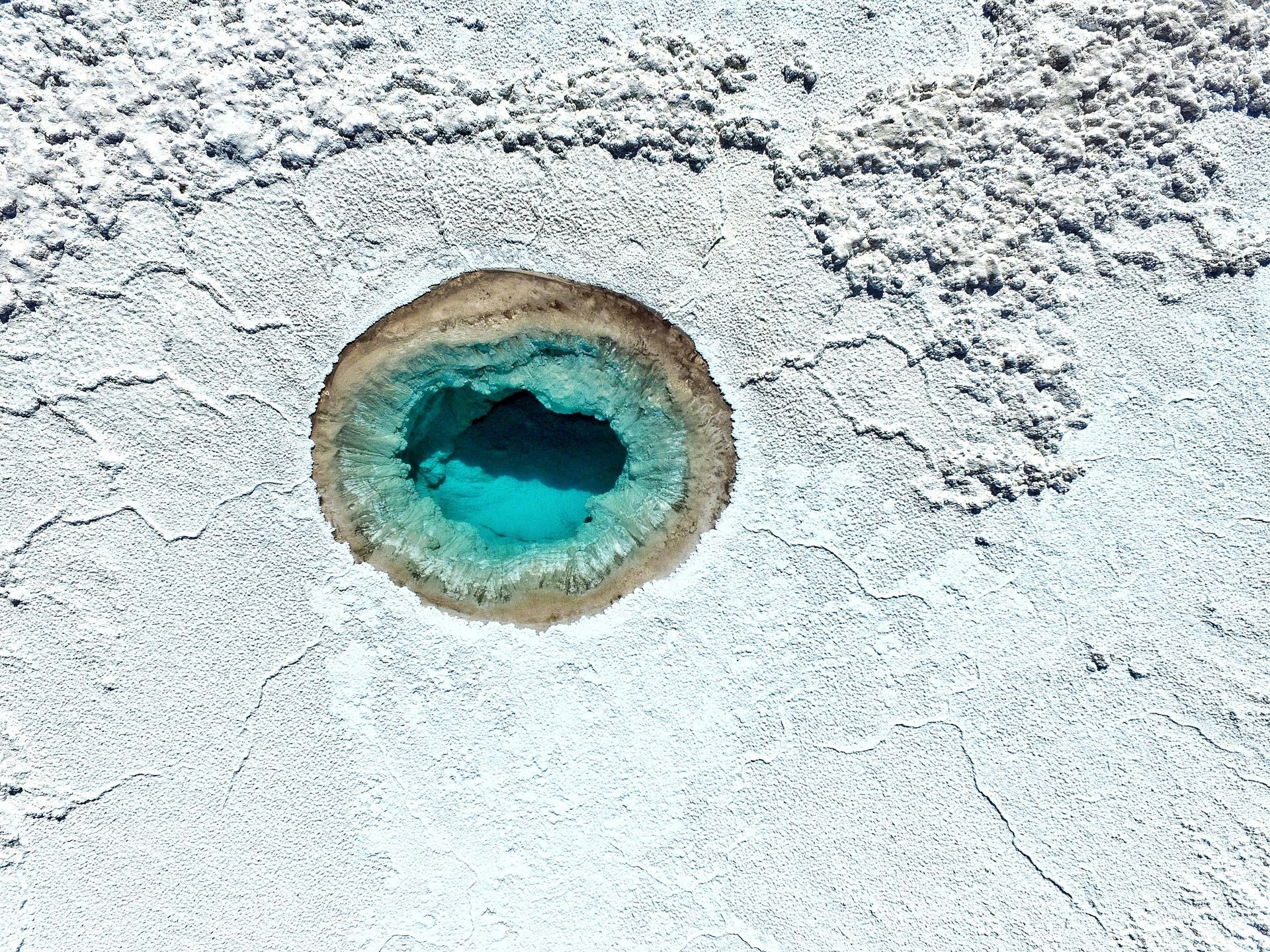 Aerial view of a turquoise hot spring surrounded by white mineral deposits in the Atacama Desert, Chile.