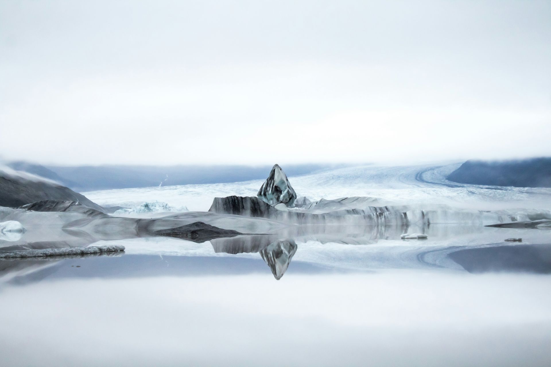 Icebergs on a reflective lake, surrounded by mist and snow-covered mountains at Vatnajökull National Park, Iceland.