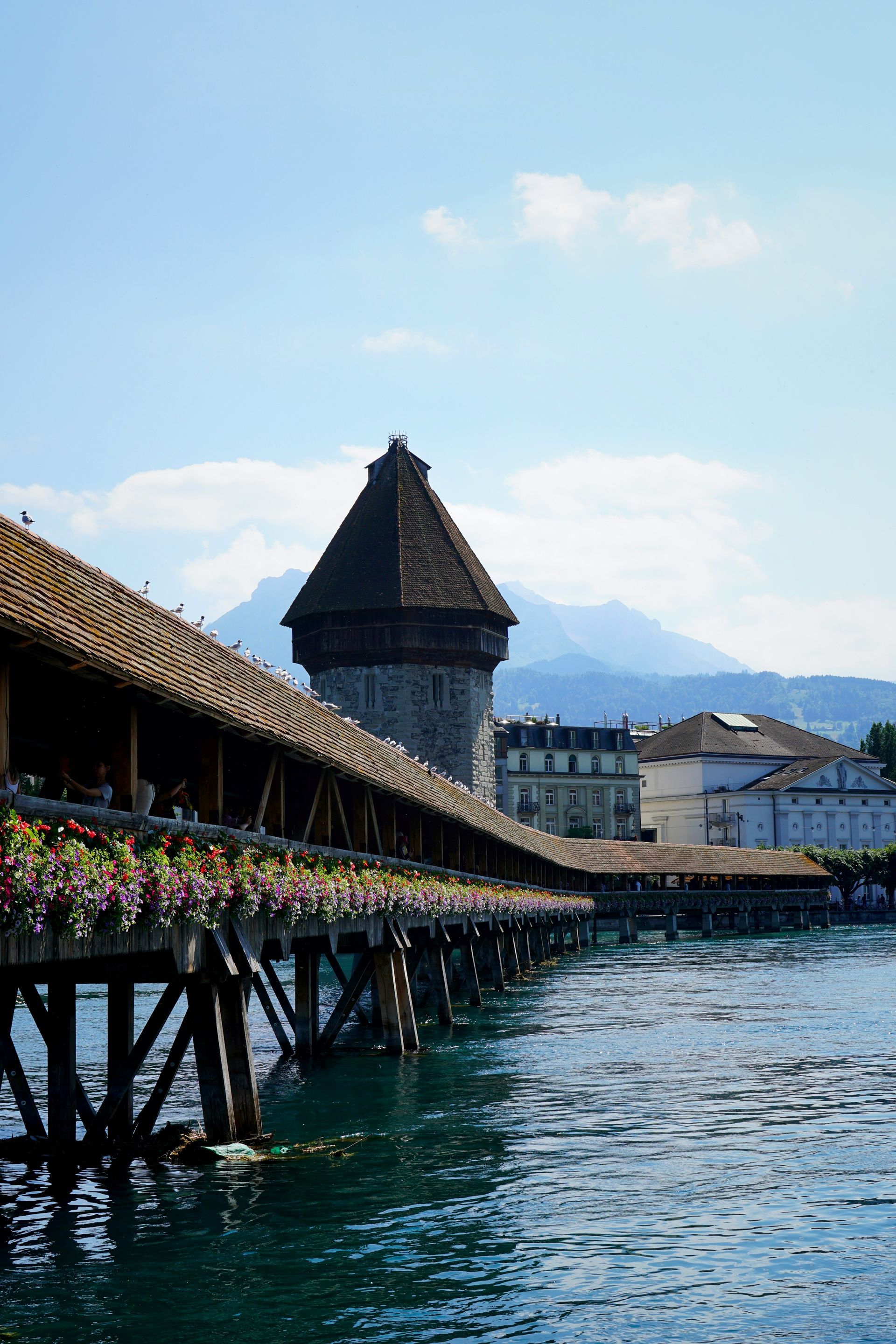 Wooden Chapel Bridge with a tower and flowers, over water in Lucerne, Switzerland.