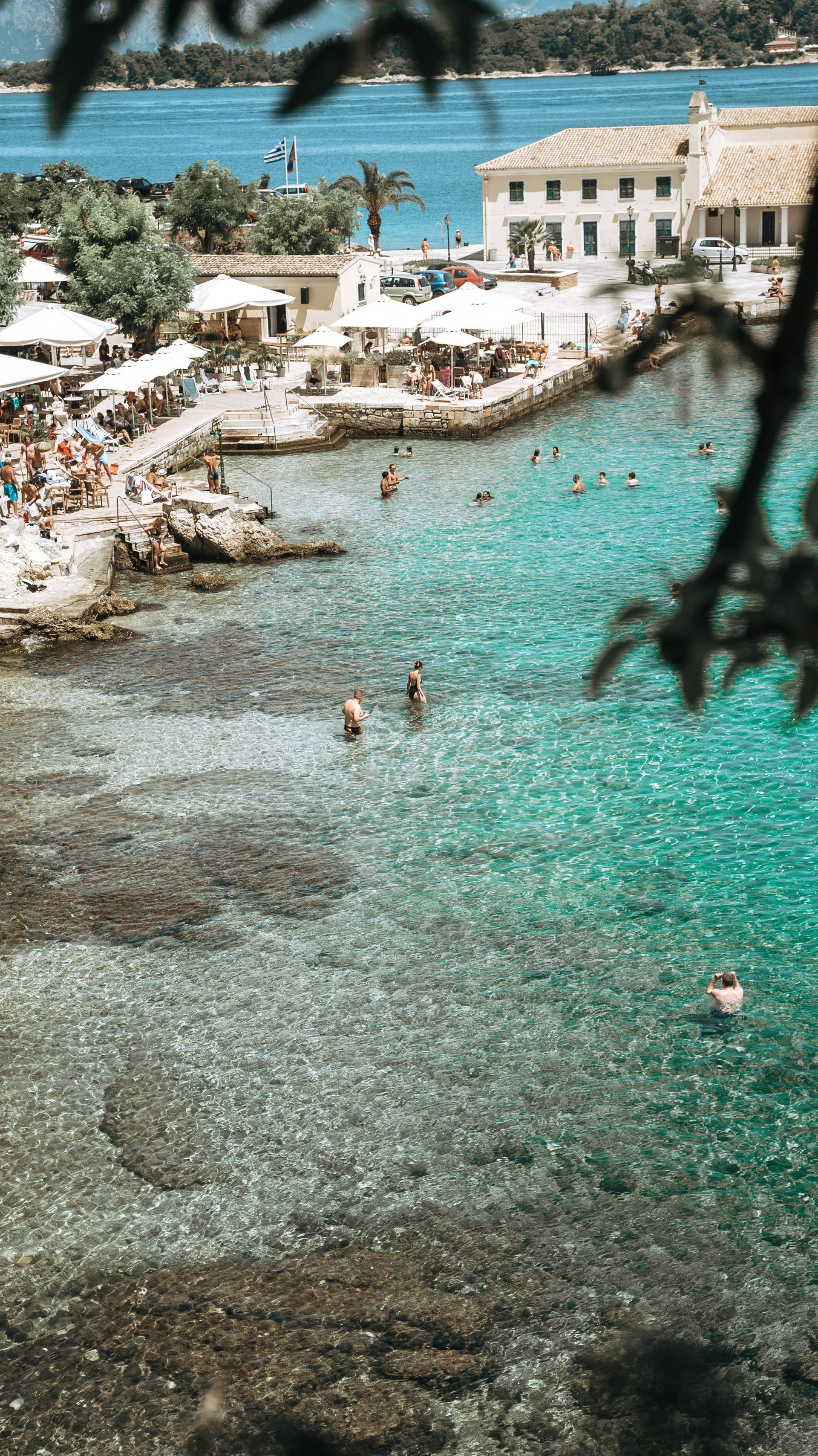 A group of people are swimming in the ocean near a beach in Corfu, Greece.