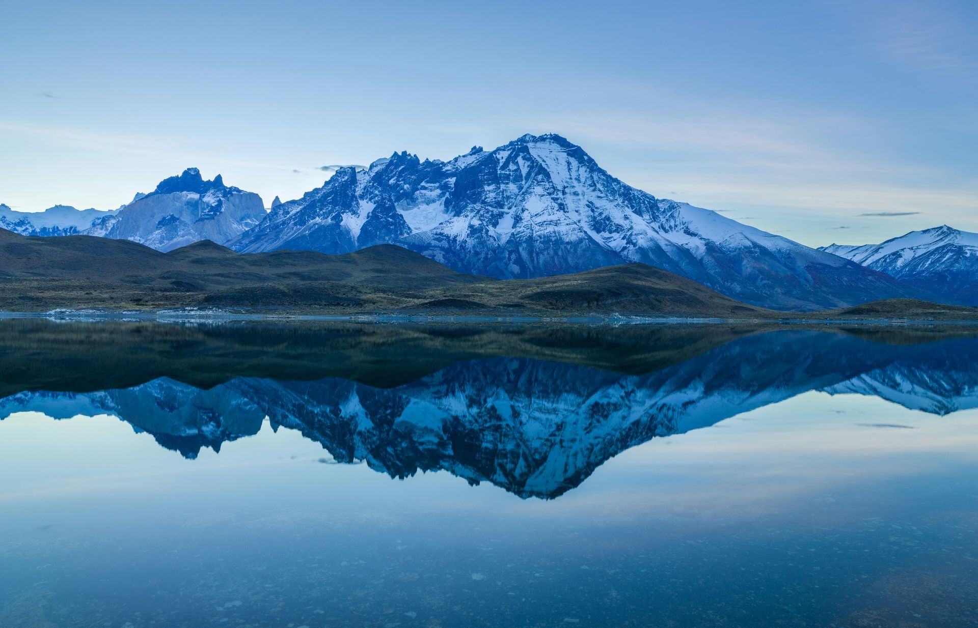 Snow-capped mountains reflected in still blue water in Patagonia, Chile.