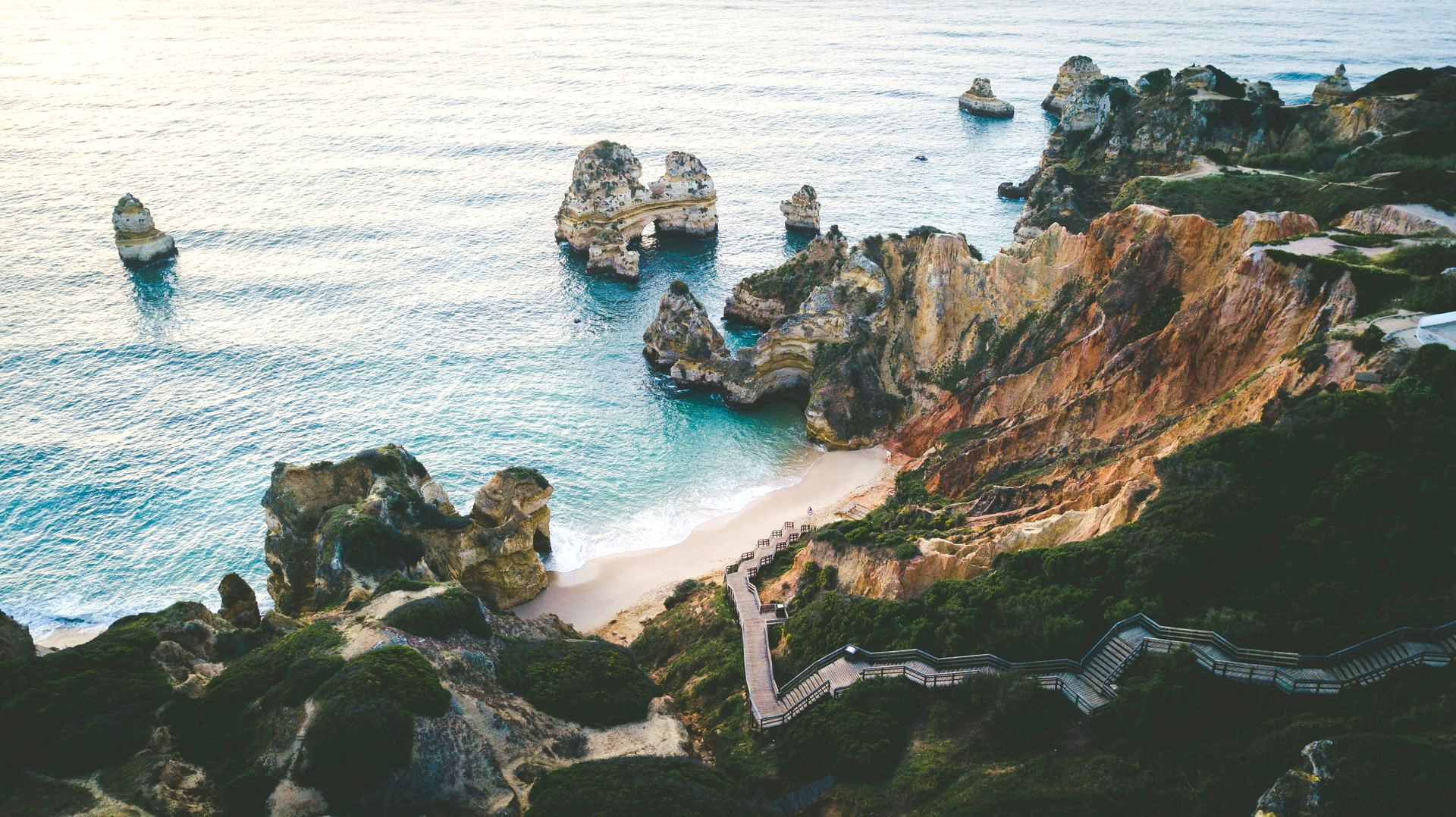 Coastal view with cliffs, beach, turquoise water, and rock formations in Lagos, Portugal.