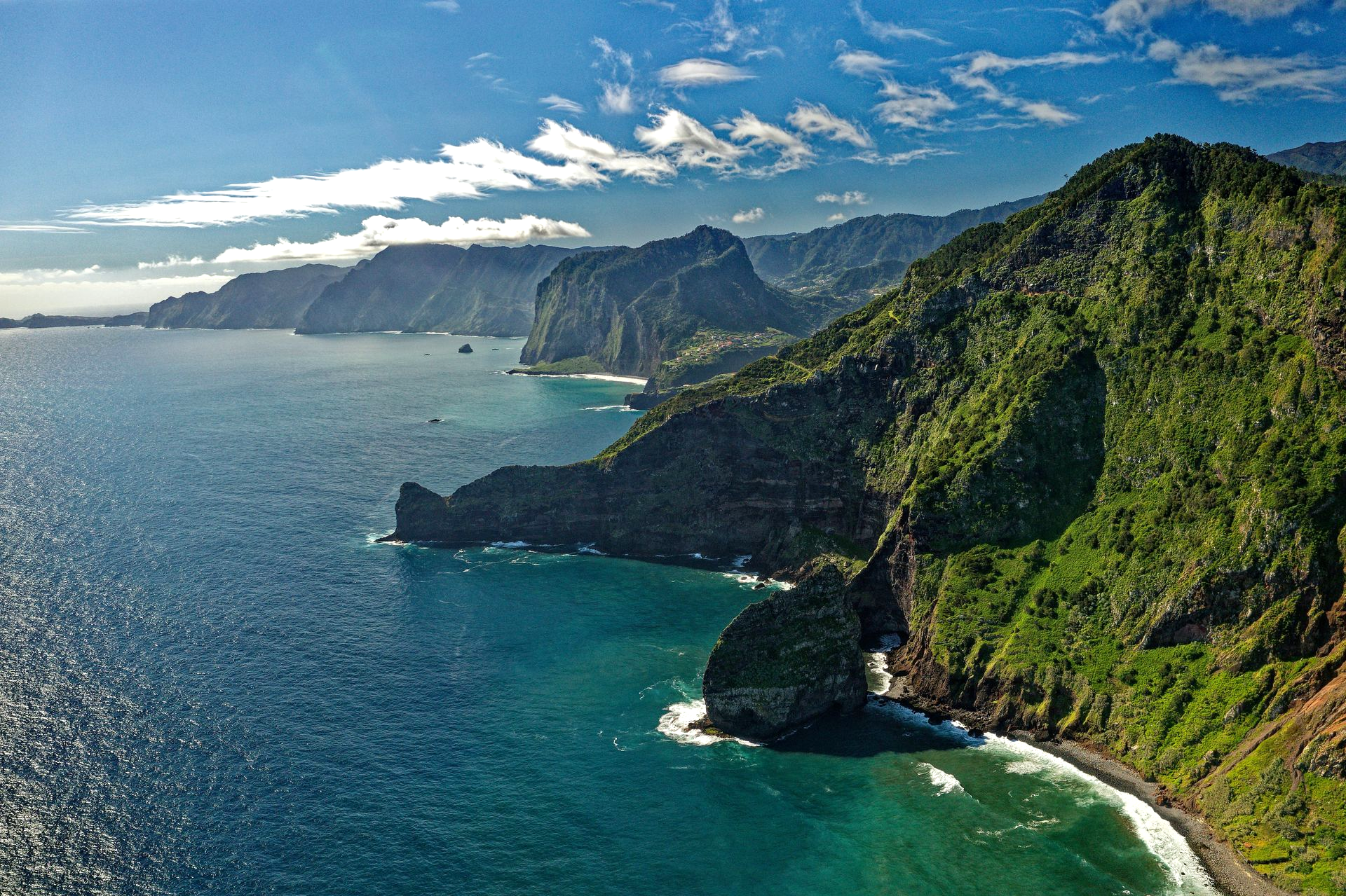 Rocky coastline with green hills meeting the deep blue ocean under a sunny sky on the island of Madeira, Portugal.