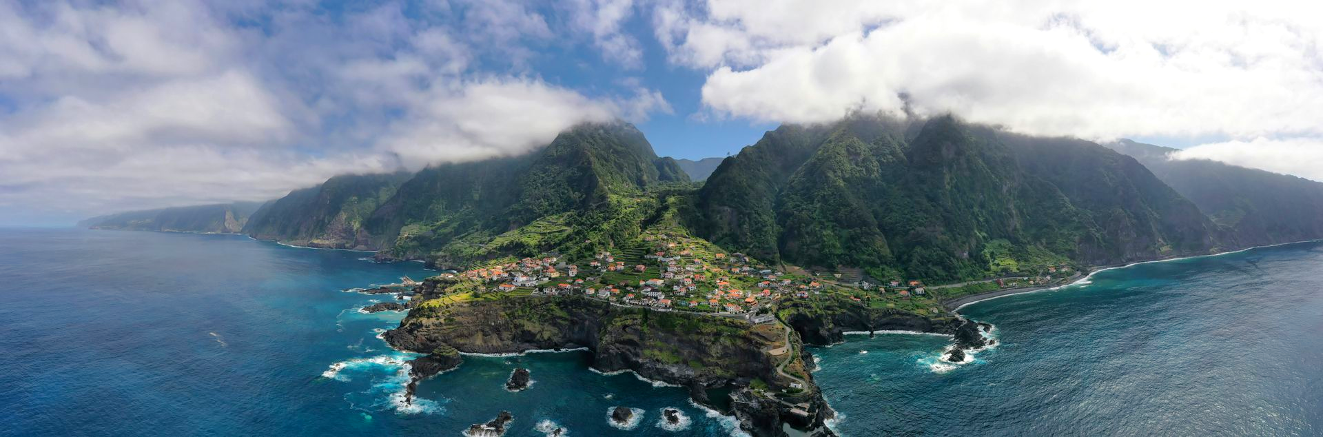 Coastal village nestled between lush green mountains and the blue ocean on the island of Madeira, Portugal.