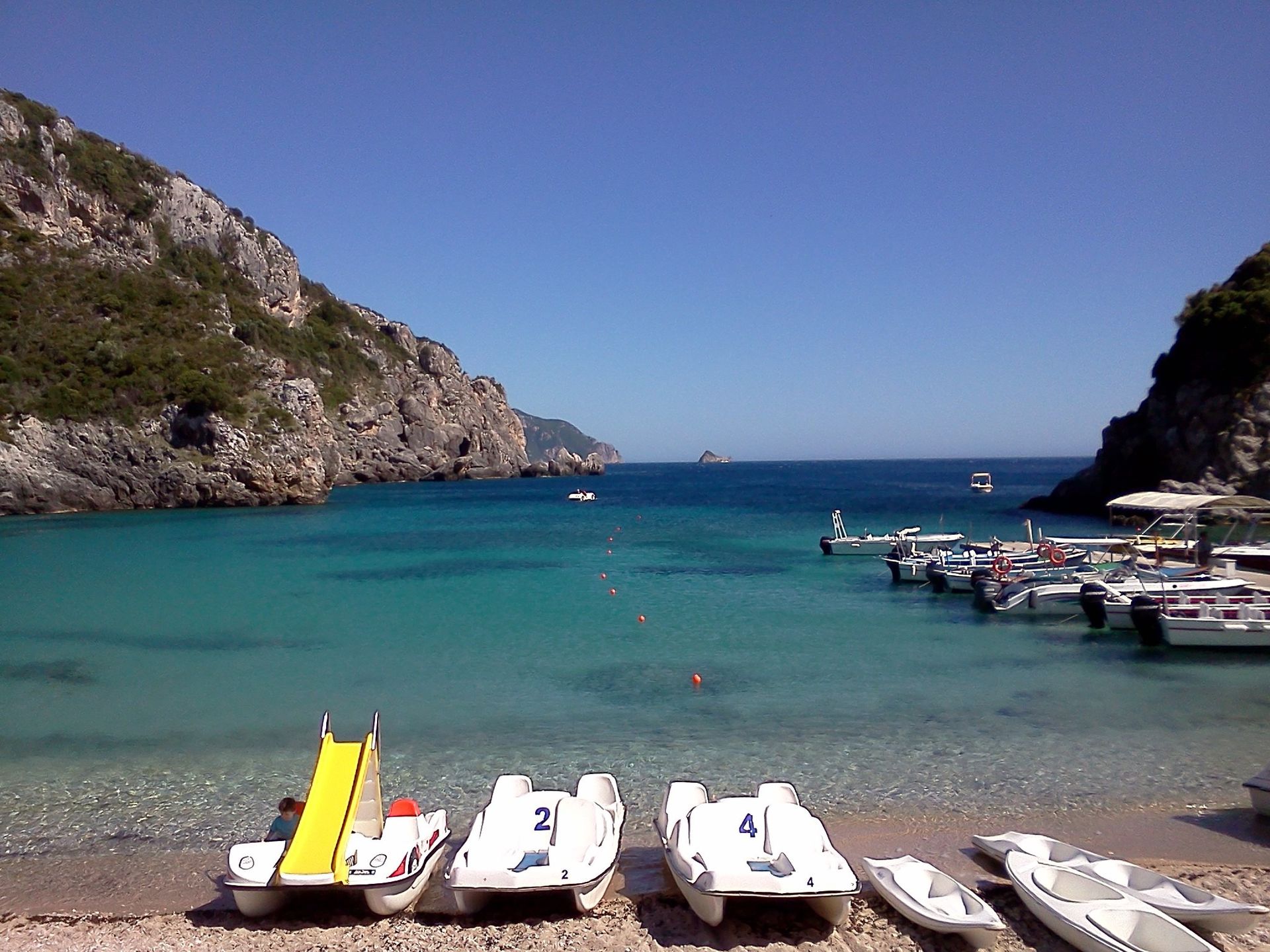Several pedal boats are lined up on a beach near the water in Corfu, Greece.
