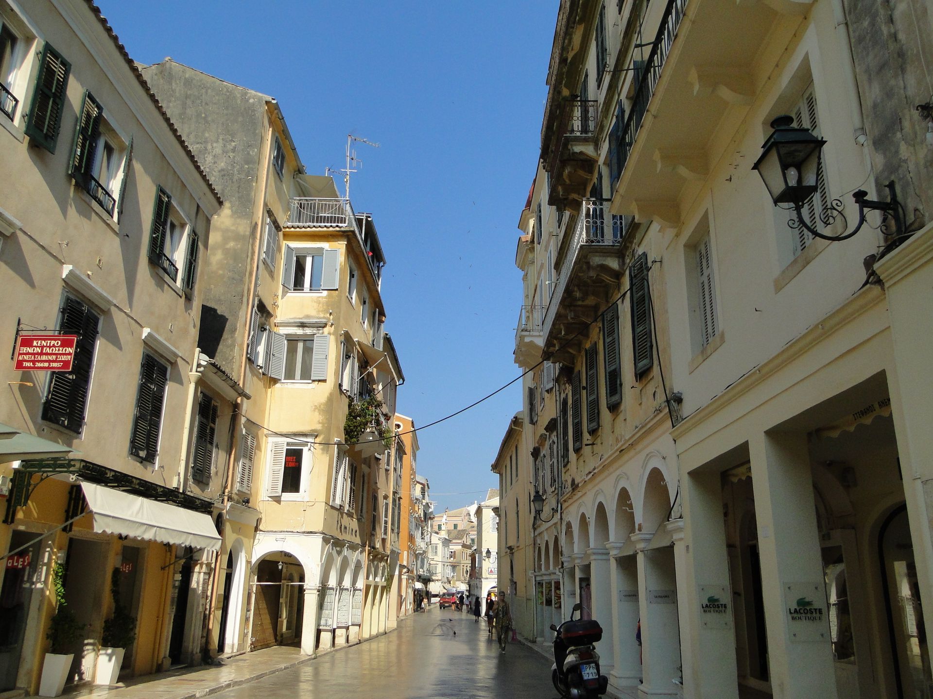 A man is riding a scooter down a narrow street between buildings in Corfu, Greece.