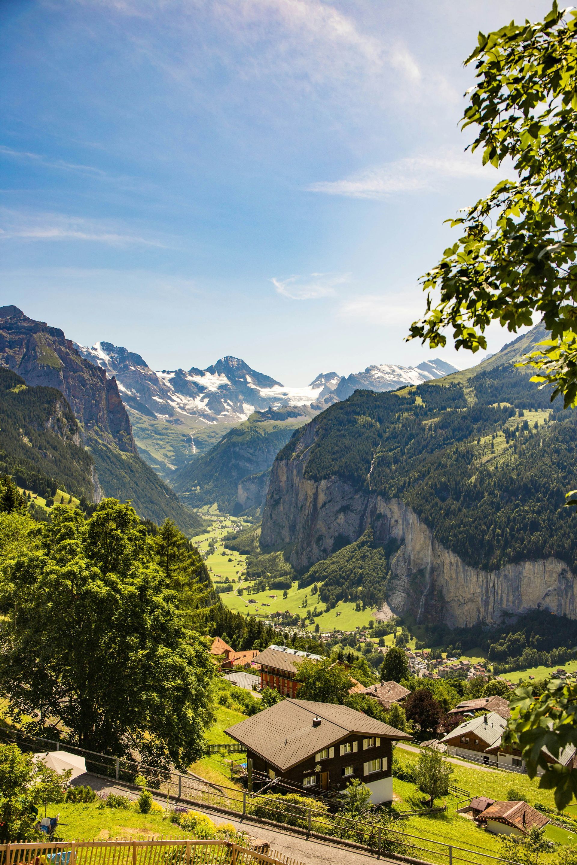 Lush green valley nestled between snow-capped mountains, with a small Swiss village and blue sky above in Lauterbrunnen.