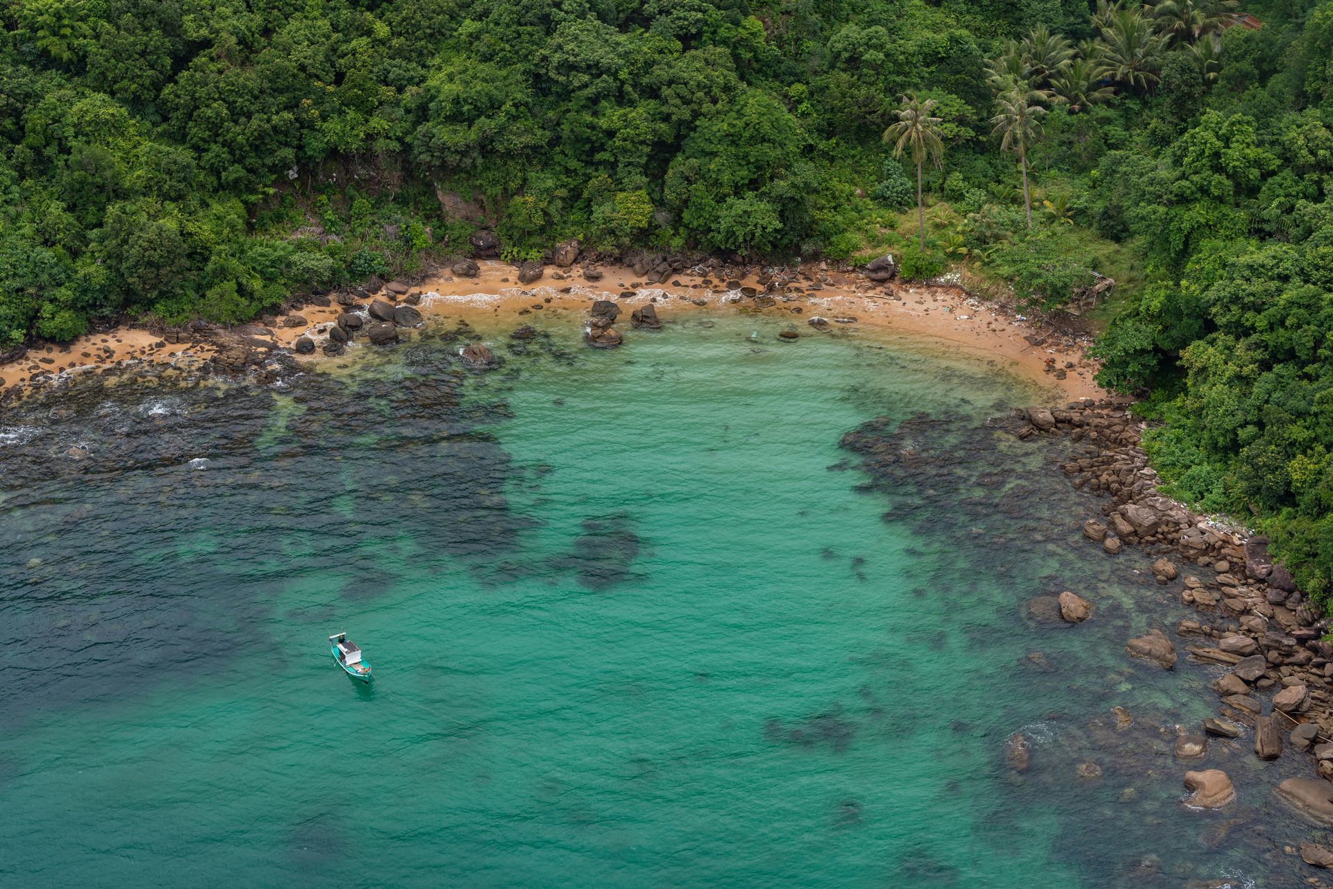 Aerial view of a small beach with clear turquoise water, surrounded by green forest in Phú Quốc, Vietnam.