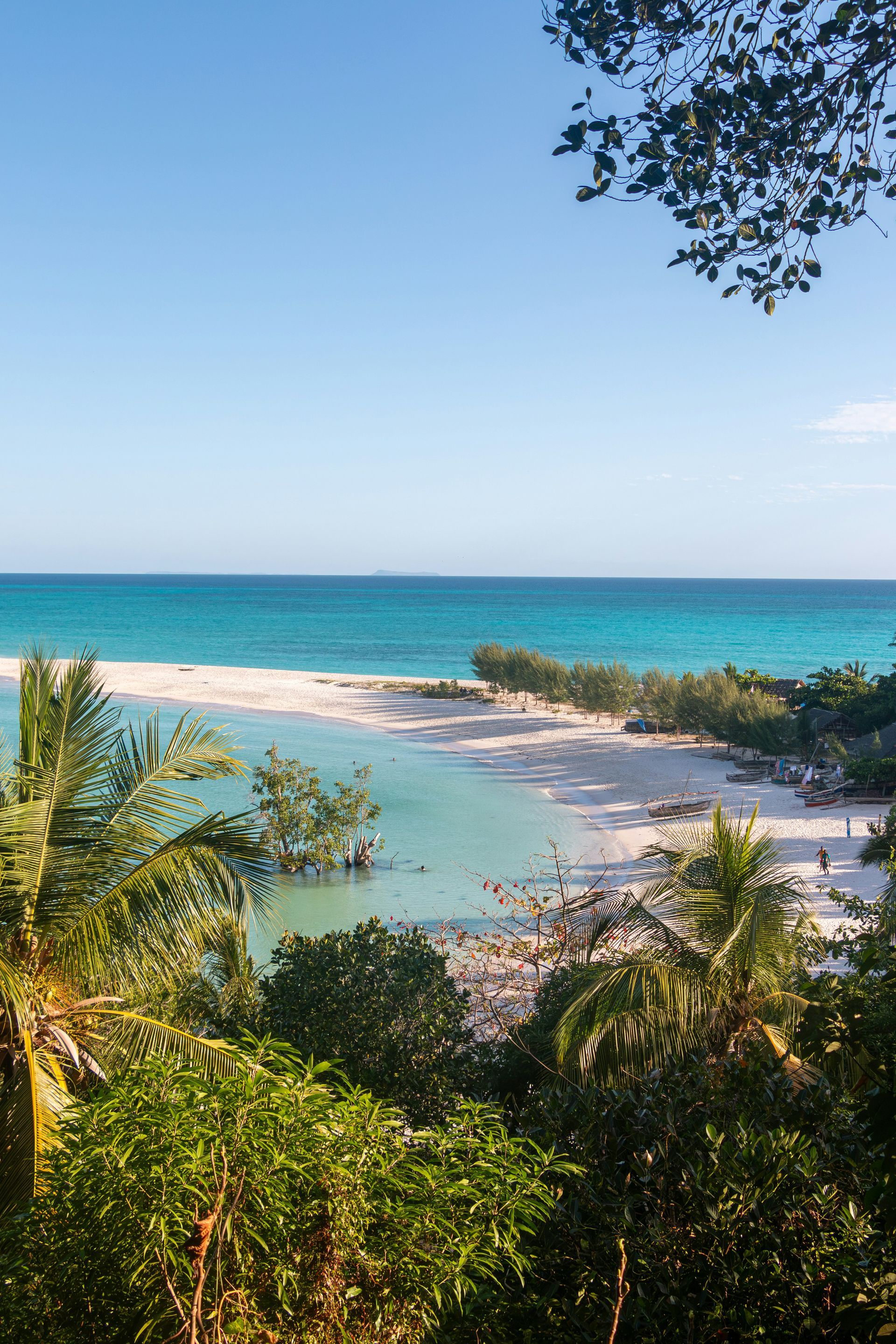 Beach with white sand and turquoise water, framed by lush green trees on Nosy Iranj, Madagascar.