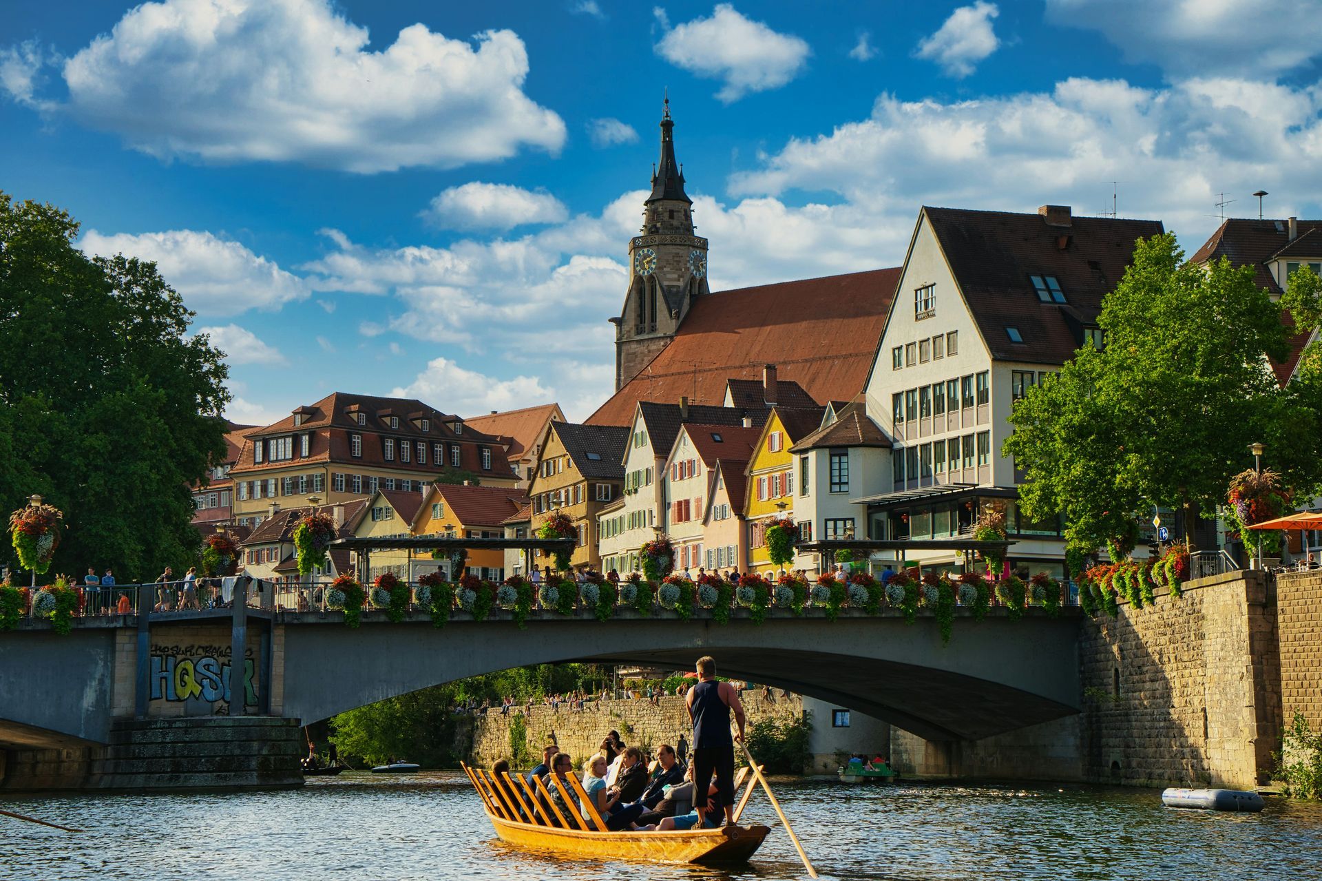 A group of people are rowing a boat down a river under a bridge in Regensburg, Germany.