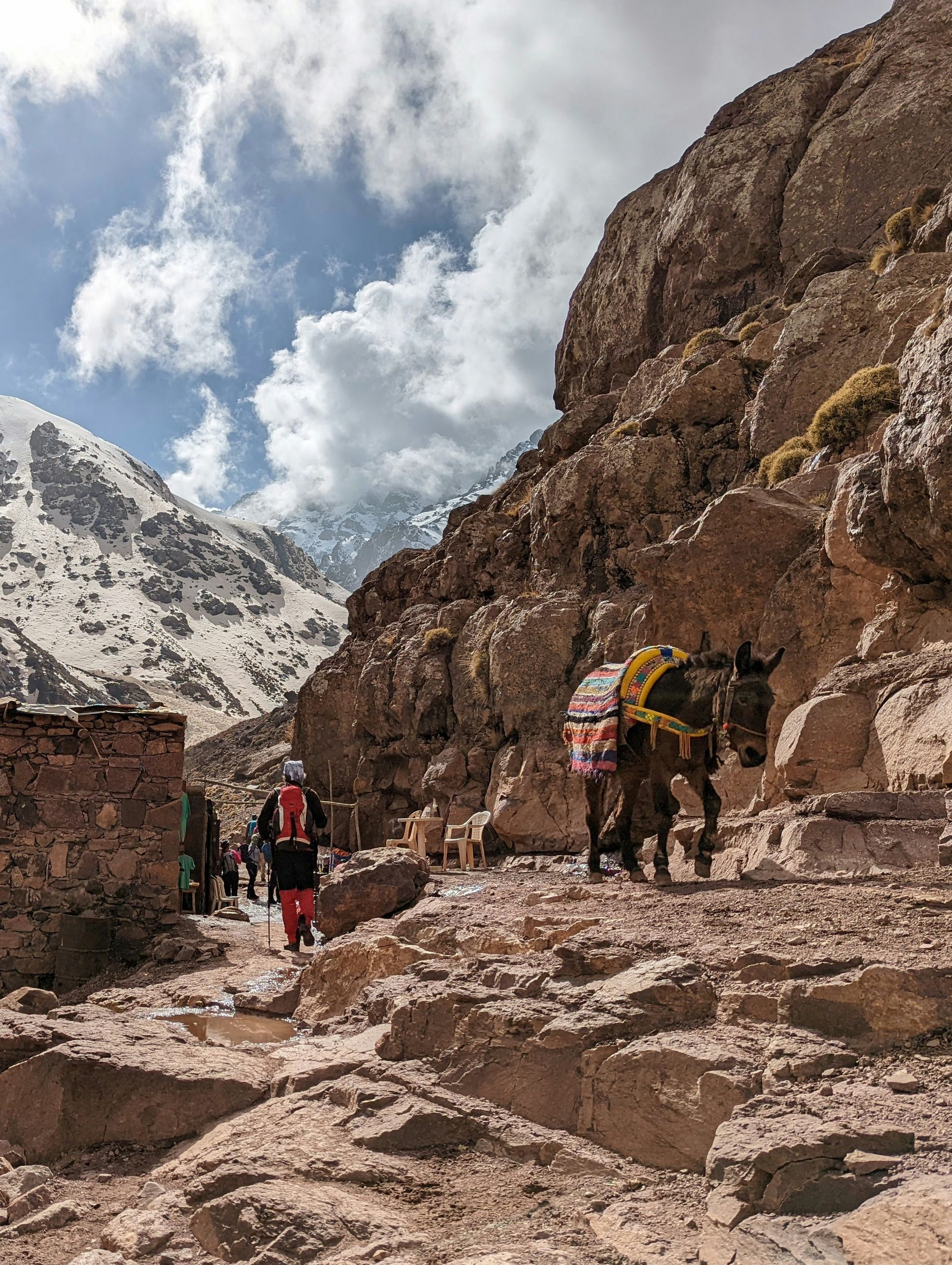 A man and a donkey are walking down a rocky path in the mountains in Toubkal, Morocco.