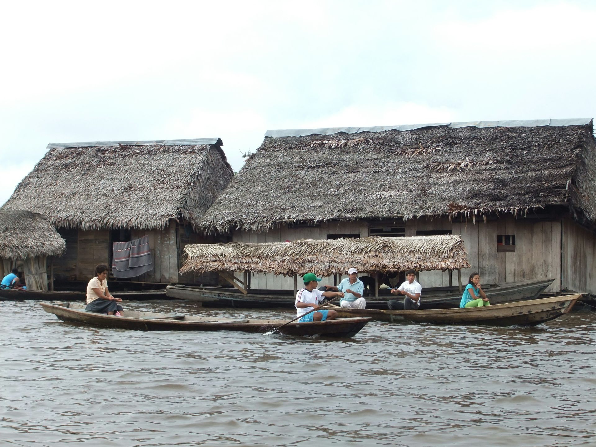 A group of people are rowing boats in the water near thatched houses in Iquitos, Peru.