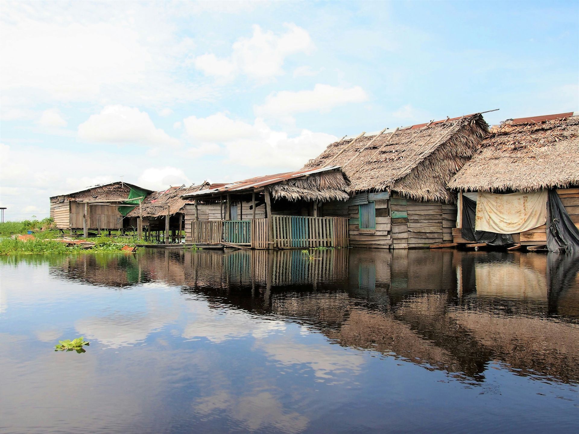 A row of houses with thatched roofs are surrounded by water in Iquitos, Peru.