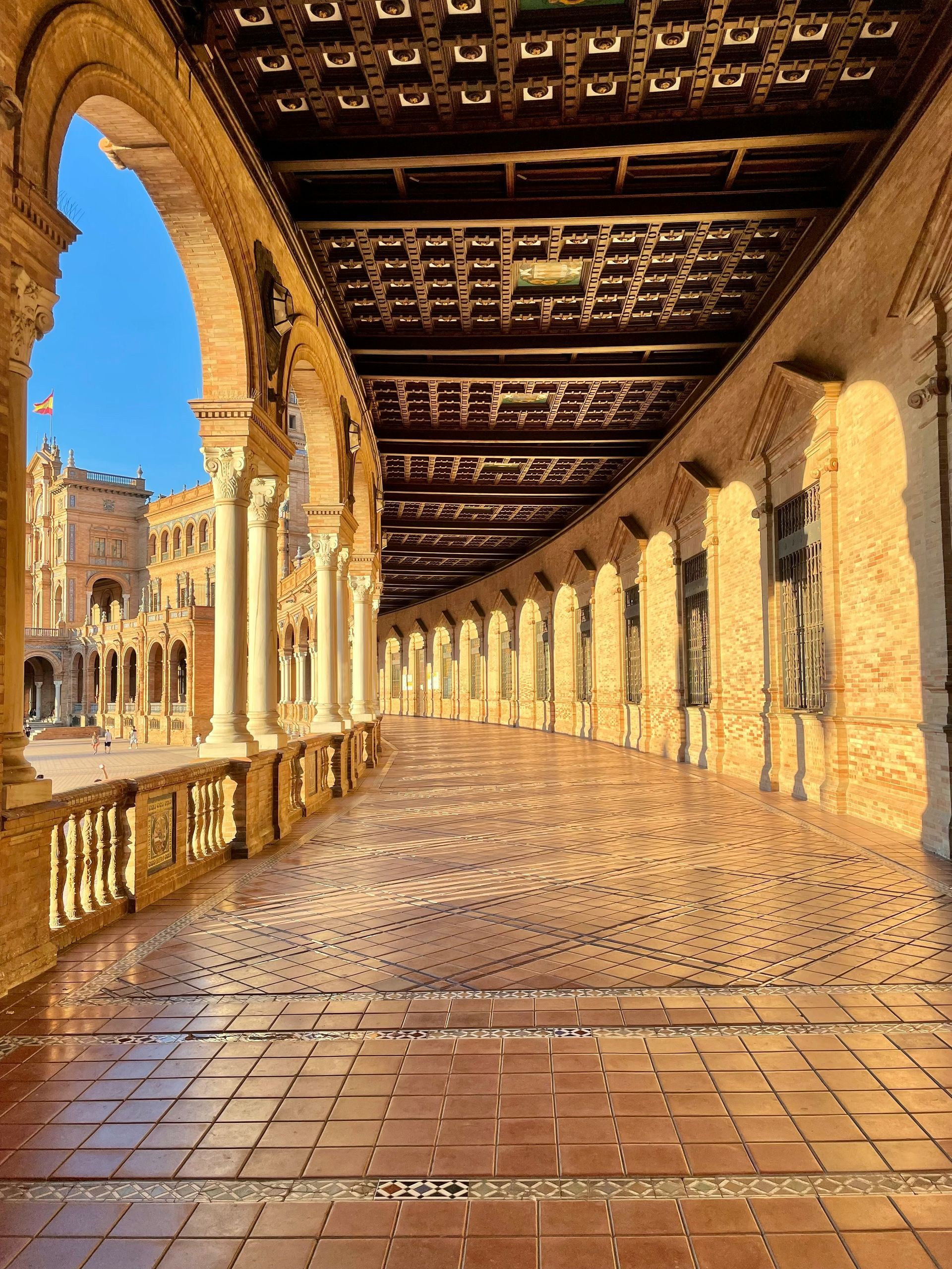 Arched walkway with columns and tile floor. Plaza de España, Seville, Spain. Golden light on the brick and tiles.
