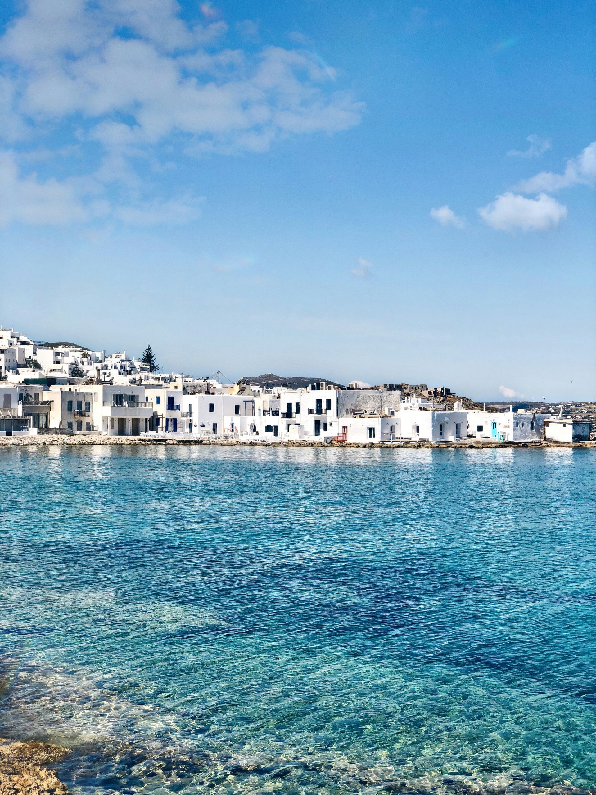A row of white houses sit on the shore of a body of water in Paros, Greece.