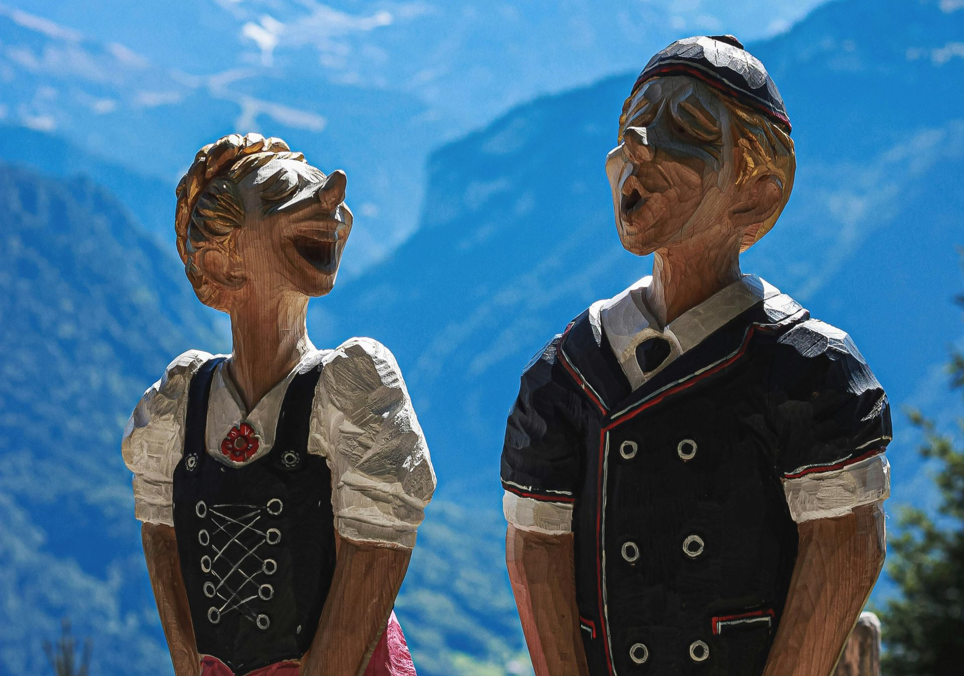 Wooden sculptures of a couple, in traditional Swiss clothing, yodeling with a mountain backdrop in Switzerland.