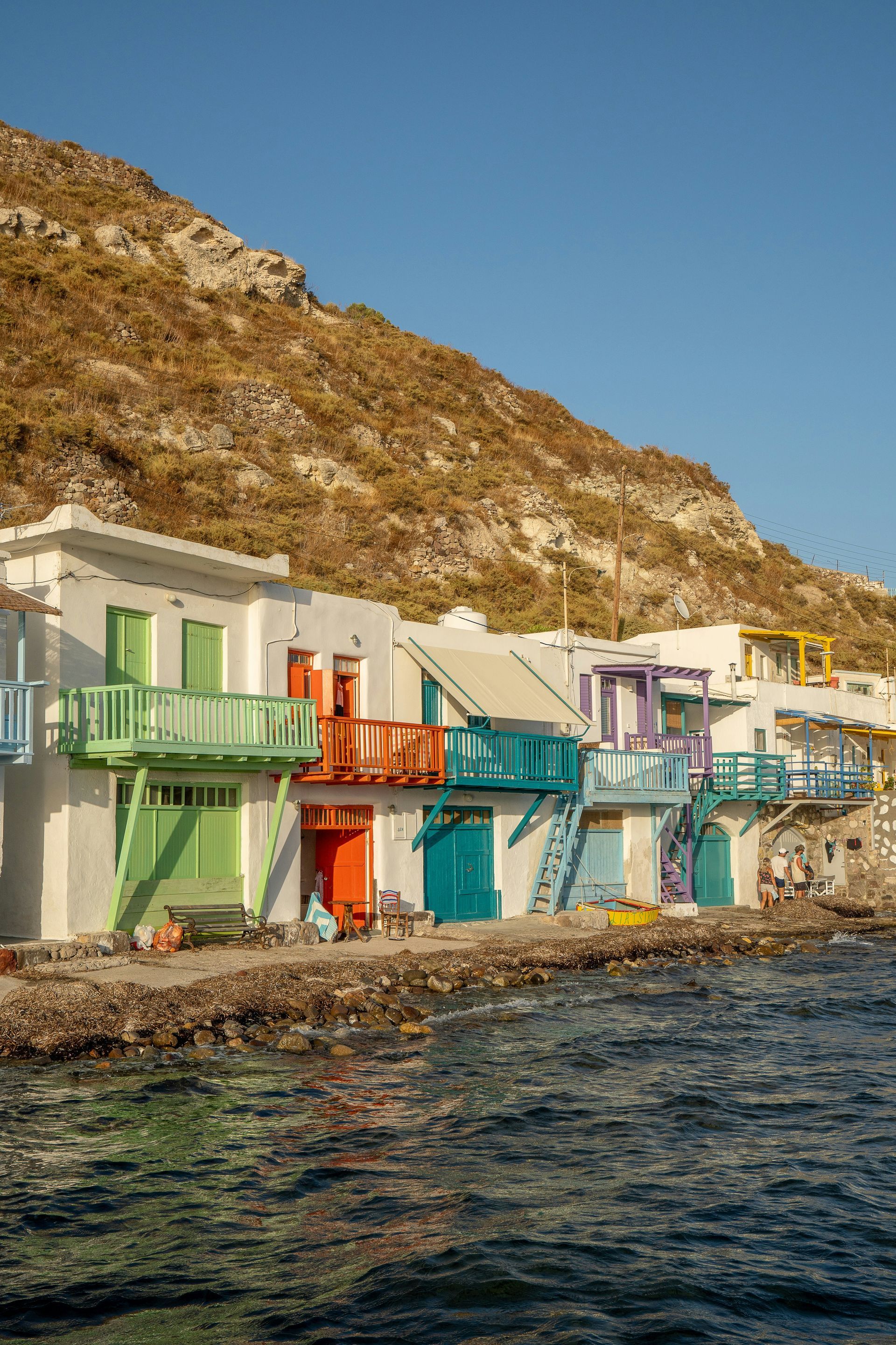 A row of colorful houses on the shore of a body of water in Milos, Greece.