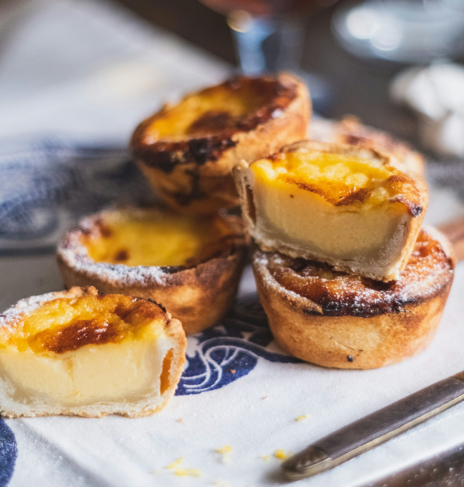 Several Pastel de Natas - crusted Portuguese custard tarts on a patterned cloth.