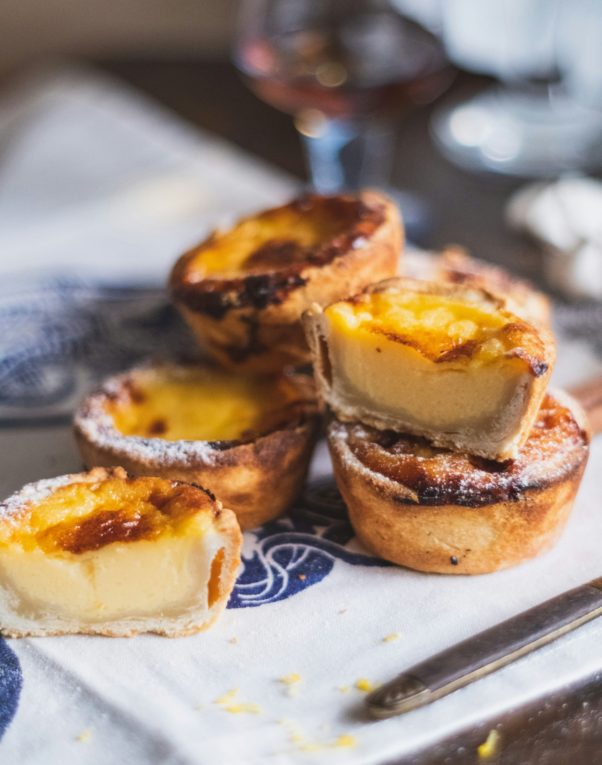 Several Pastel de Natas - crusted Portuguese custard tarts on a patterned cloth.