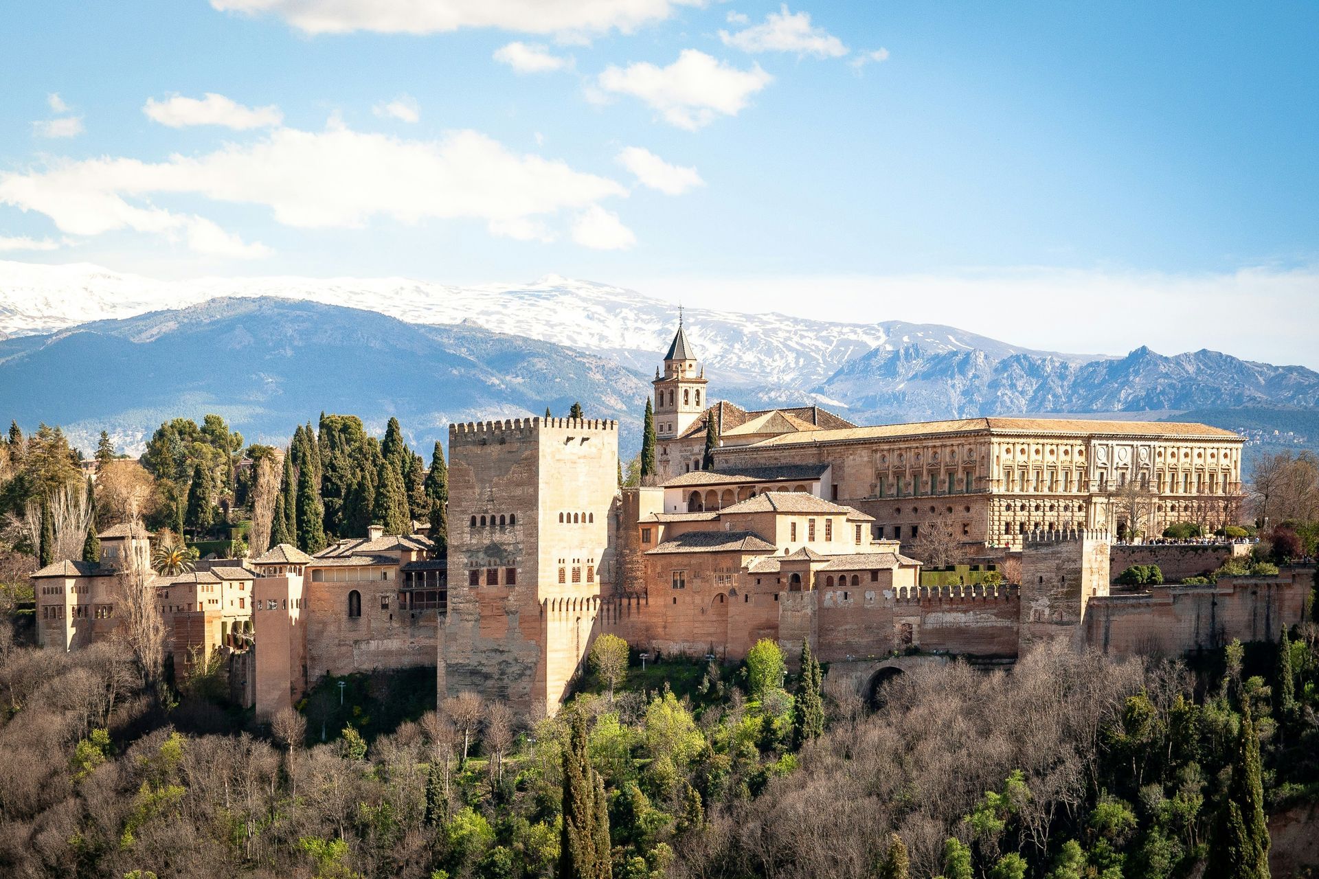Ancient Alhambra palace complex in Granada, Spain, with snow-capped mountains in the background under a blue sky.