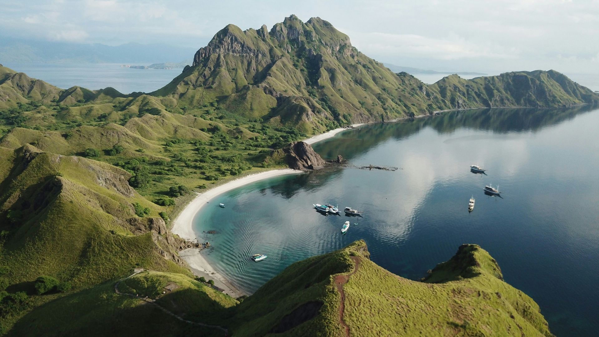 An aerial view of a tropical island with boats in the water and mountains in the background in Komodo, Indonesia.
