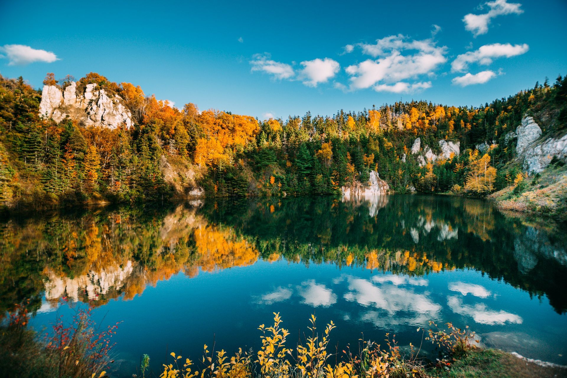 A tranquil lake reflects a vibrant autumn landscape of trees and rock formations in Nova Scotia, Canada.