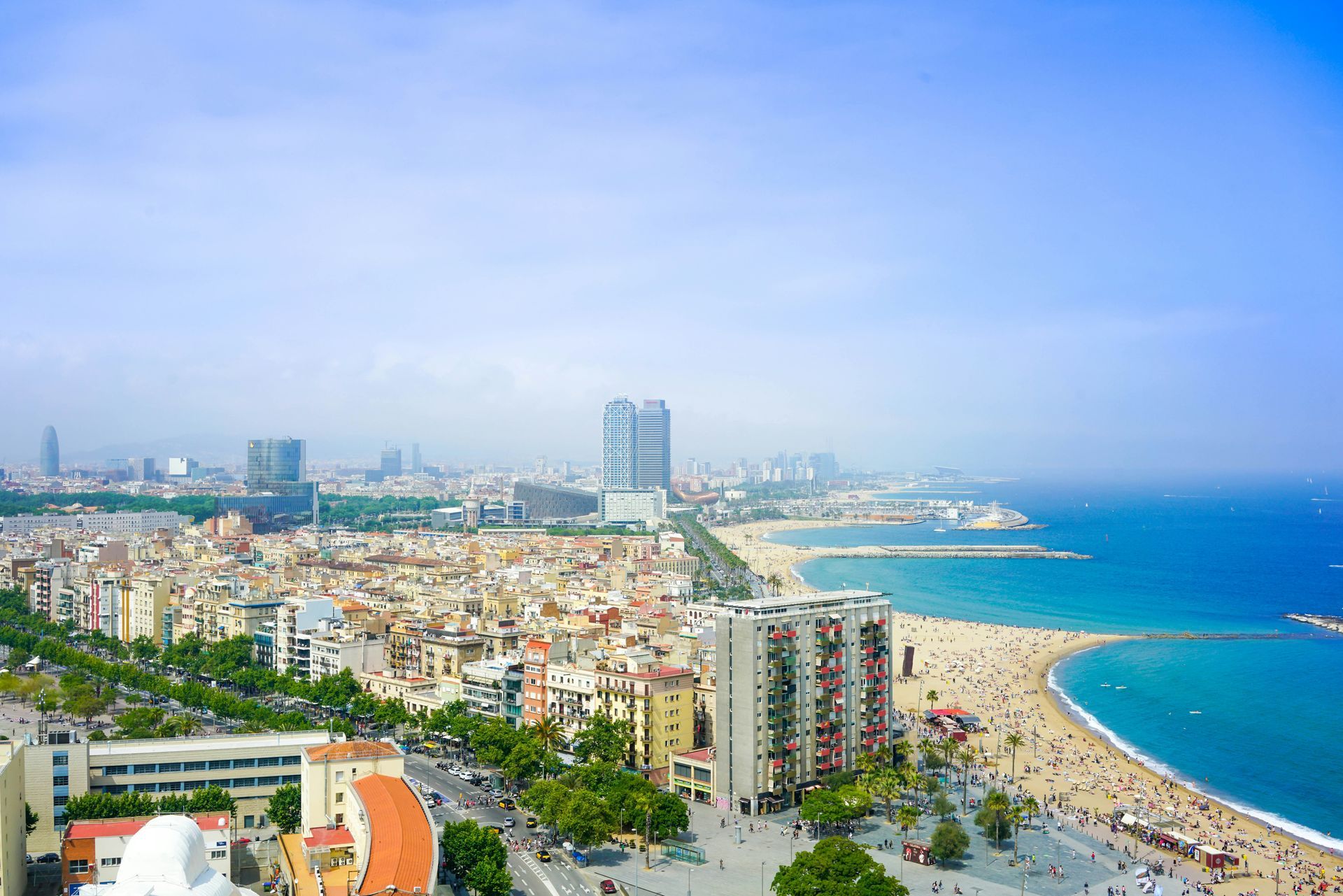 Barcelona cityscape, beach, and Mediterranean Sea under a bright blue sky.