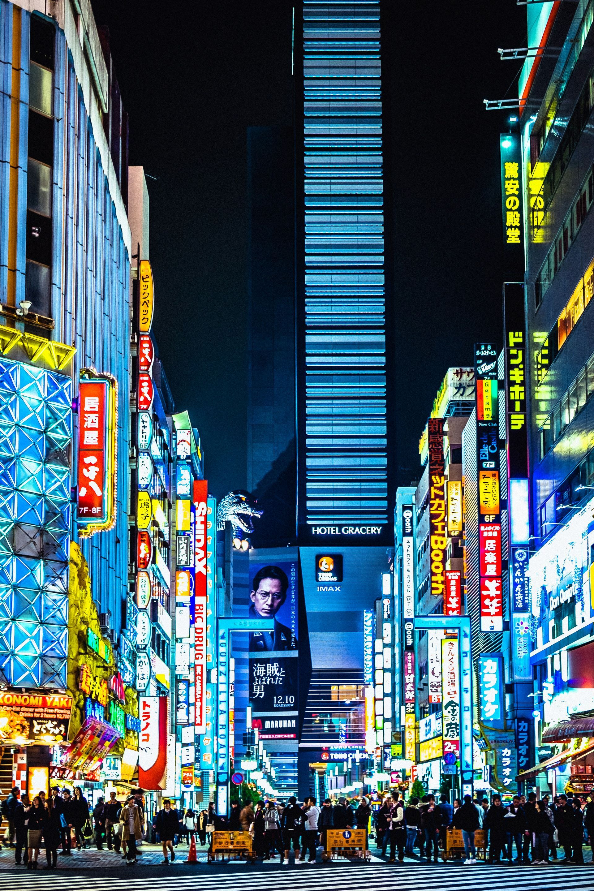 Nighttime street in Tokyo, Japan, lined with vibrant neon signs and a tall skyscraper.