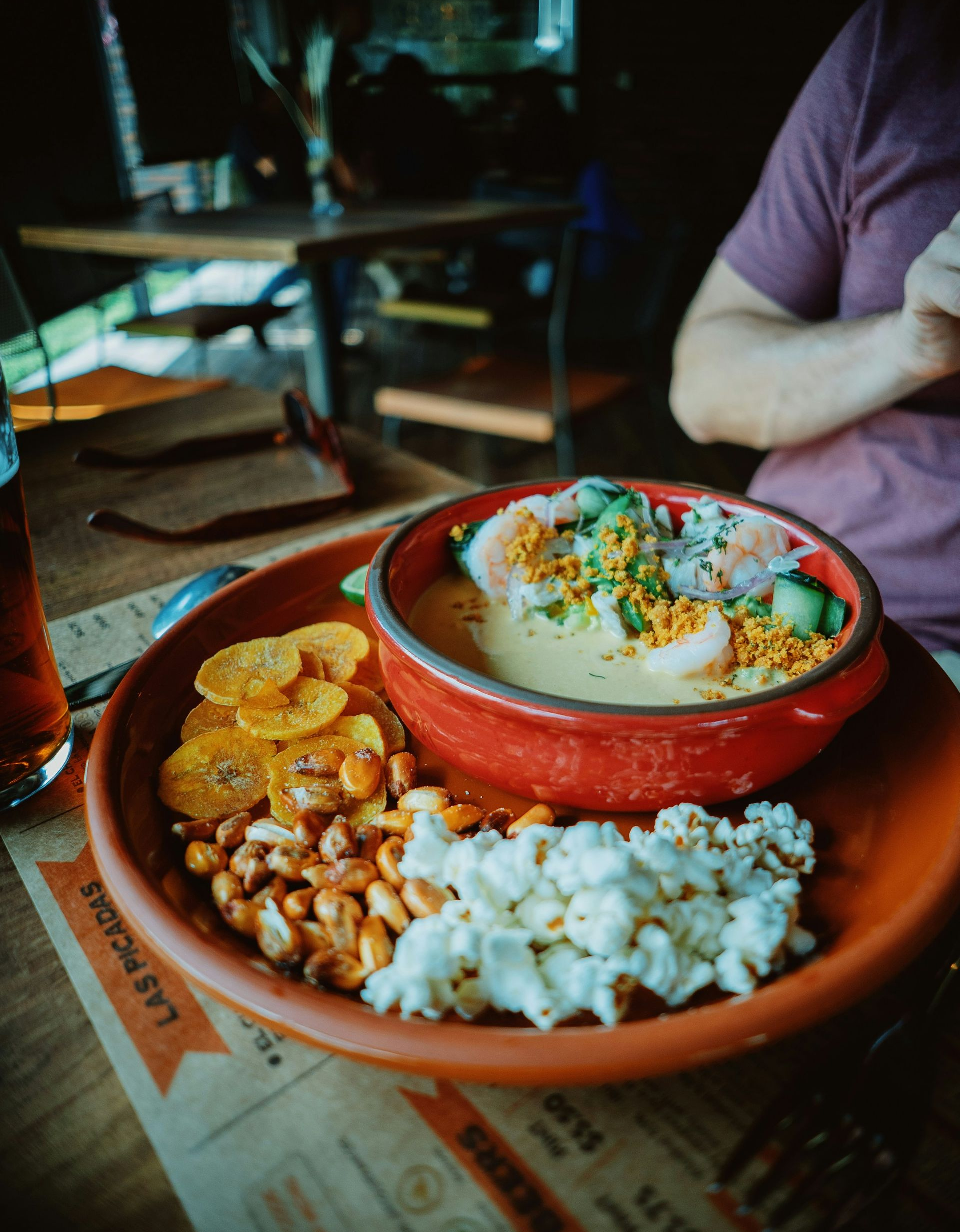 Bowl of ceviche with side snacks, person reaching into view at table in Ecuador.