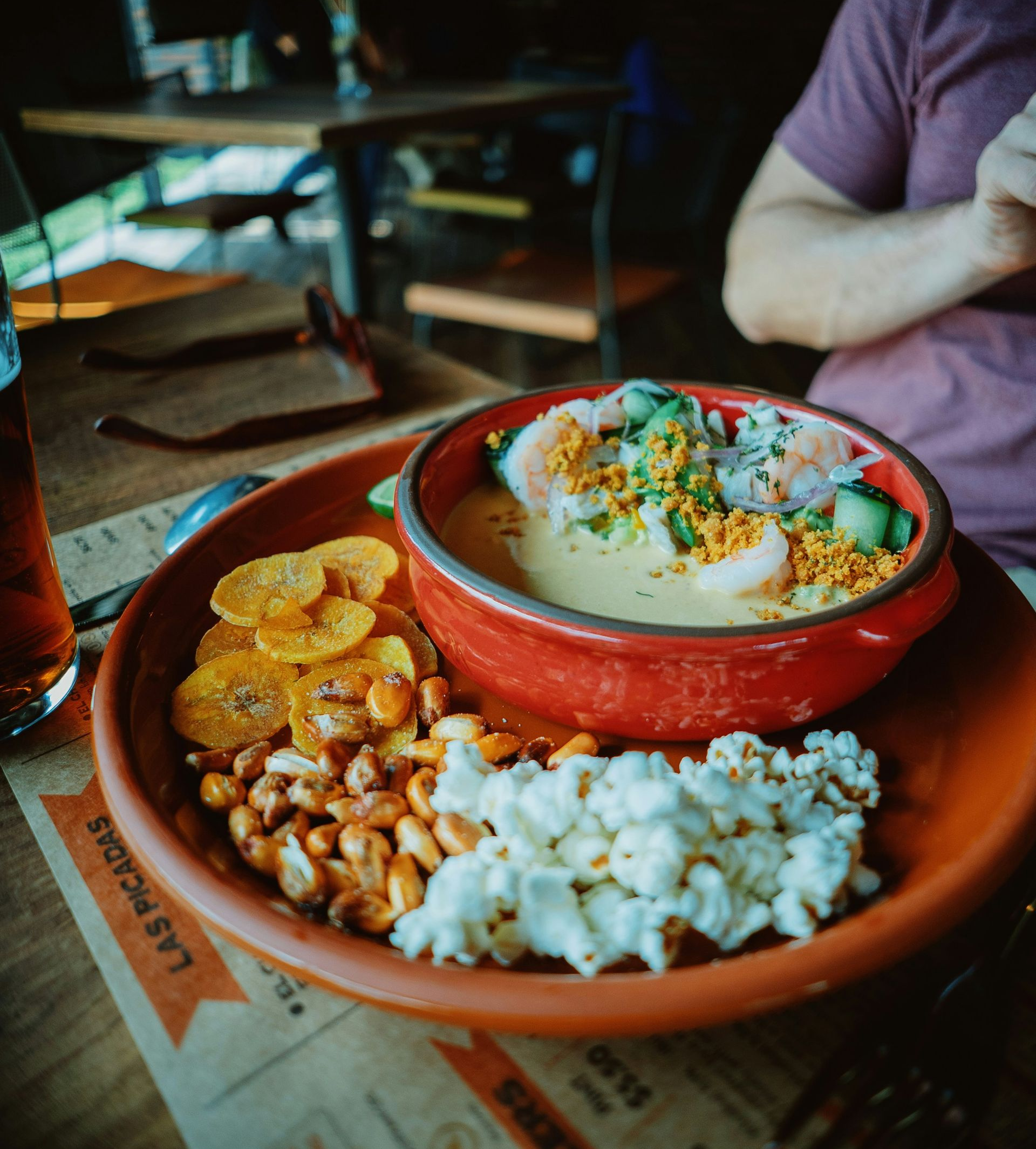 Bowl of ceviche with side snacks, person reaching into view at table in Ecuador.